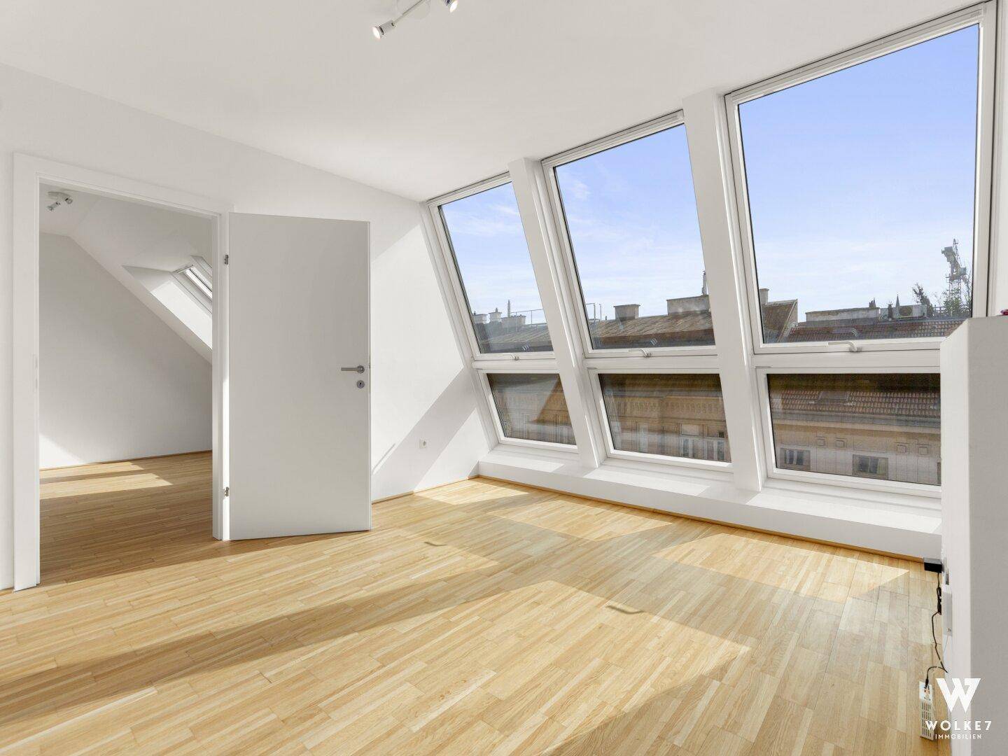 Heller Raum mit Holzboden, Dachschrägen und großen Fenstern, ideal als Wohn- oder Arbeitsbereich.