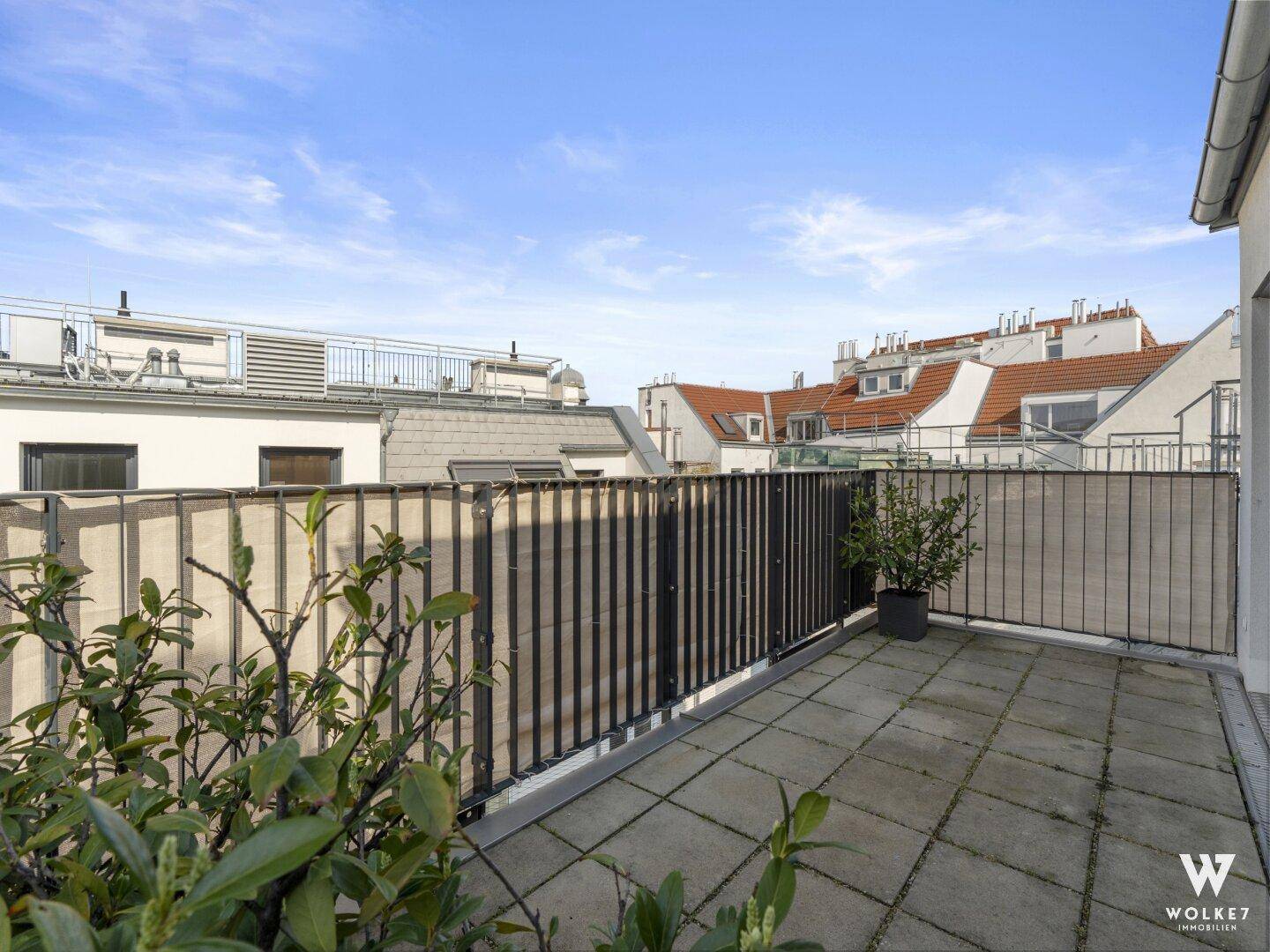 Geräumige Dachterrasse mit Fliesenboden und Blick über die umliegenden Dächer der Stadt.