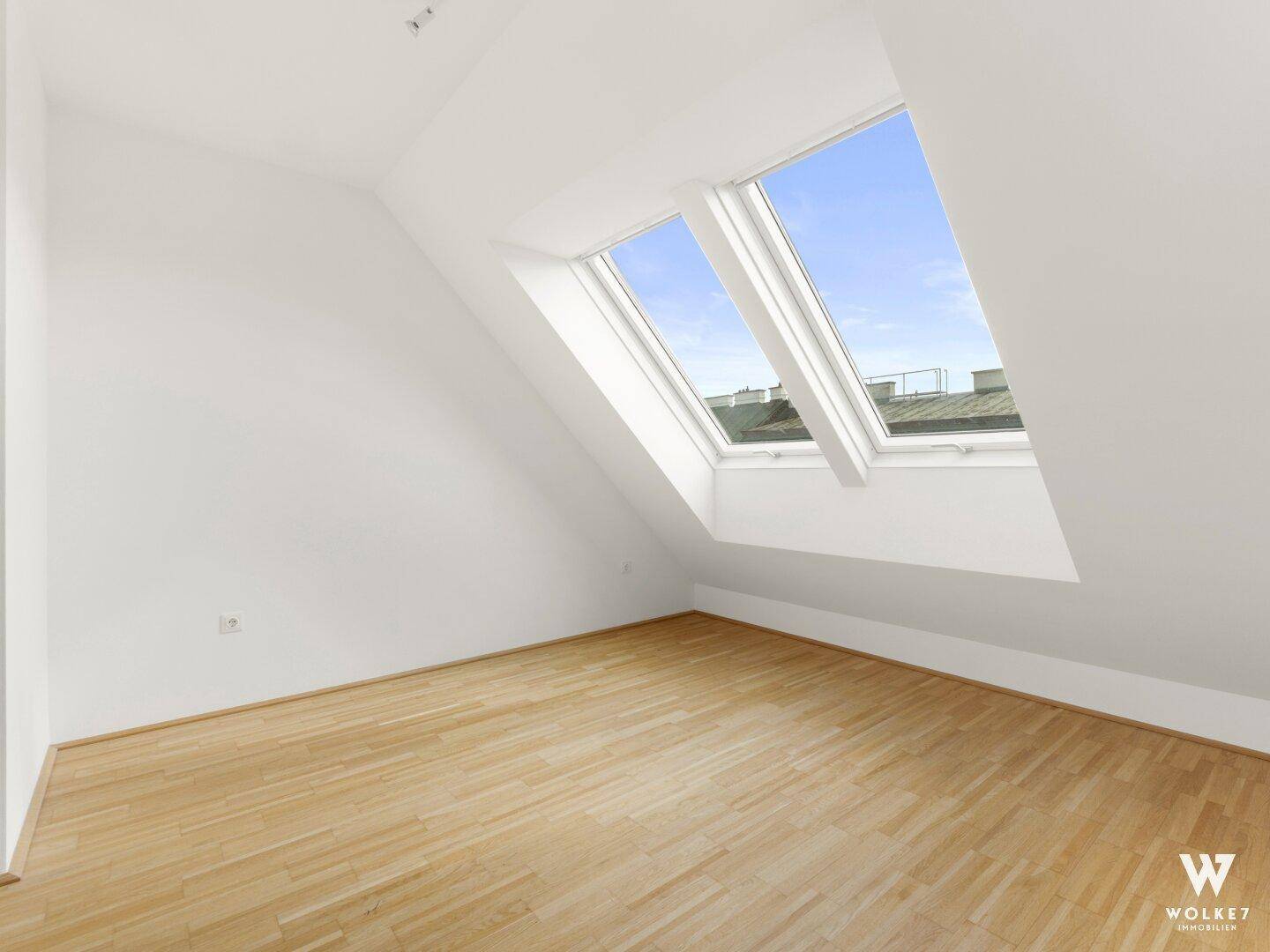 Leeres Zimmer mit Holzboden, Dachschrägen und zwei großen Dachfenstern für optimale Belichtung.