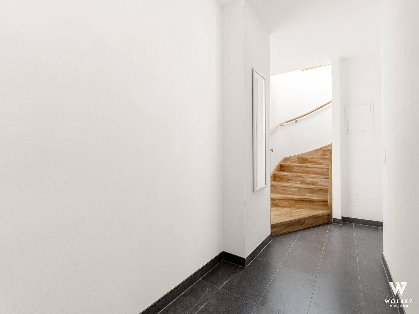 Heller Flur mit dunklem Fliesenboden und einer eleganten Holztreppe, die in die obere Etage führt.