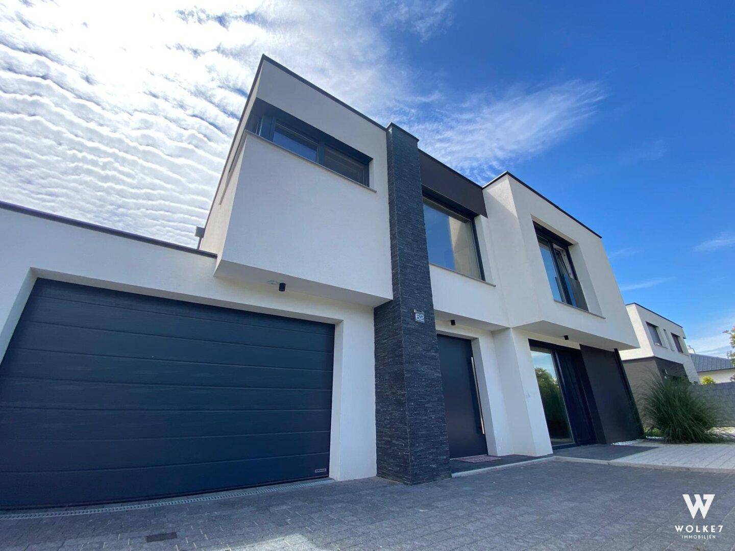 Moderne Hausfassade mit integrierter Doppelgarage und gepflasterter Auffahrt unter blauem Himmel.