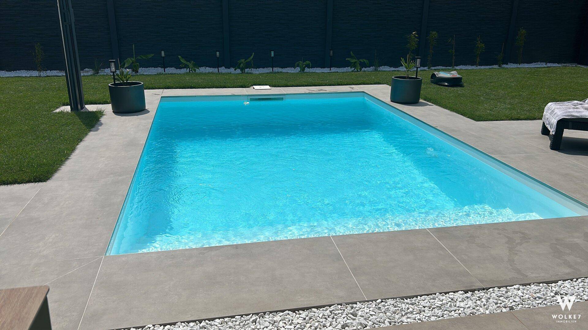 Moderner, rechteckiger Swimmingpool im Gartenbereich mit sauberer Fliesenumrandung und Kiesstreifen.