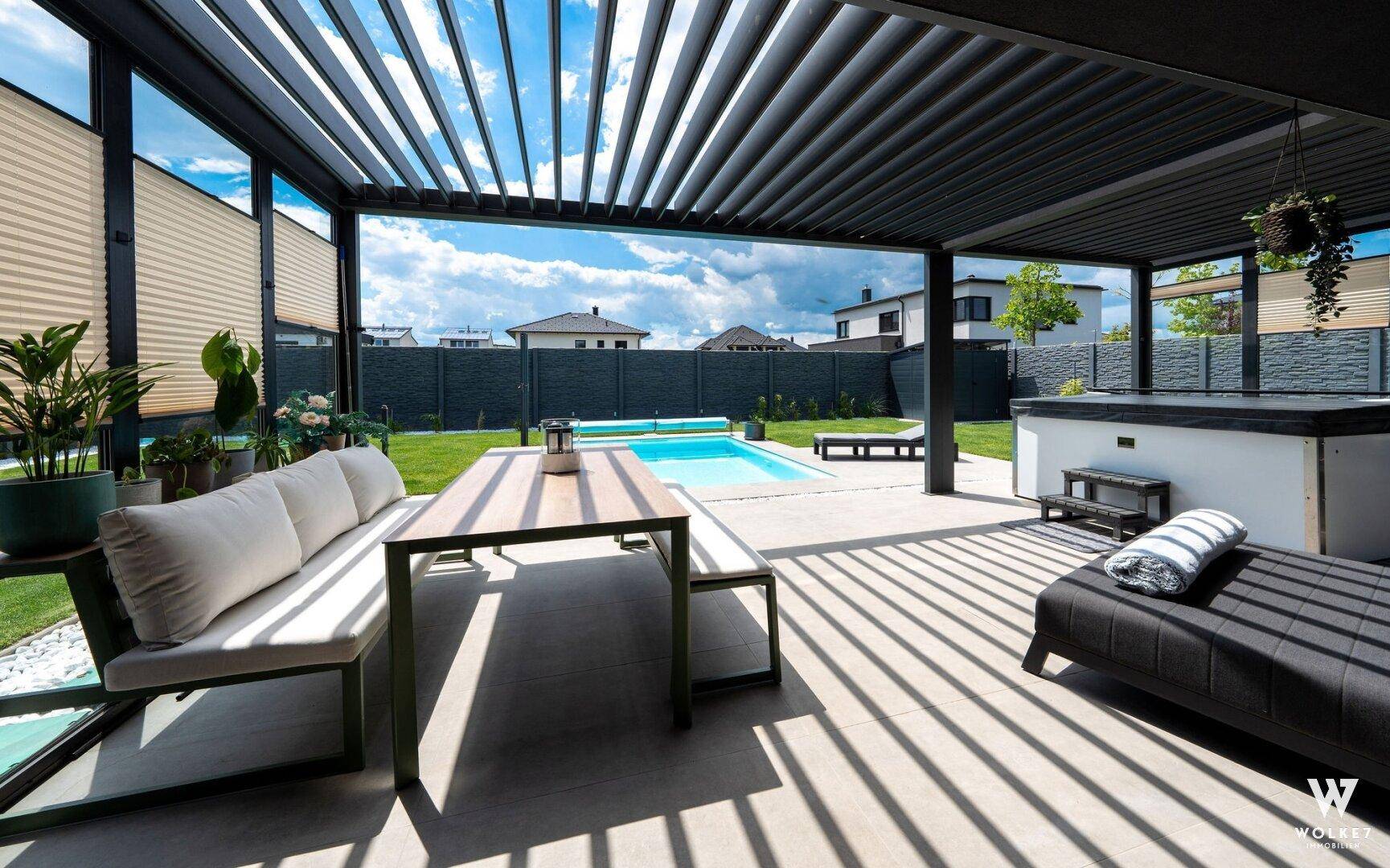 Überdachte Terrasse mit Loungemöbeln, Esstisch und Blick auf den Pool und Whirlpool im Garten.