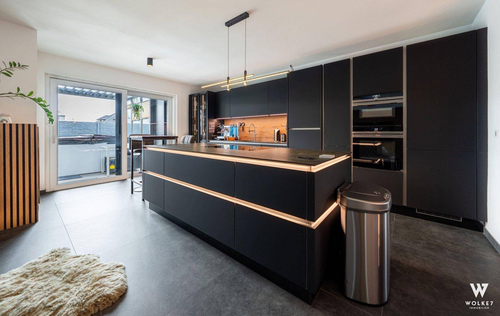 Elegante schwarze Einbauküche mit beleuchteter Kücheninsel und Zugang zur Terrasse.