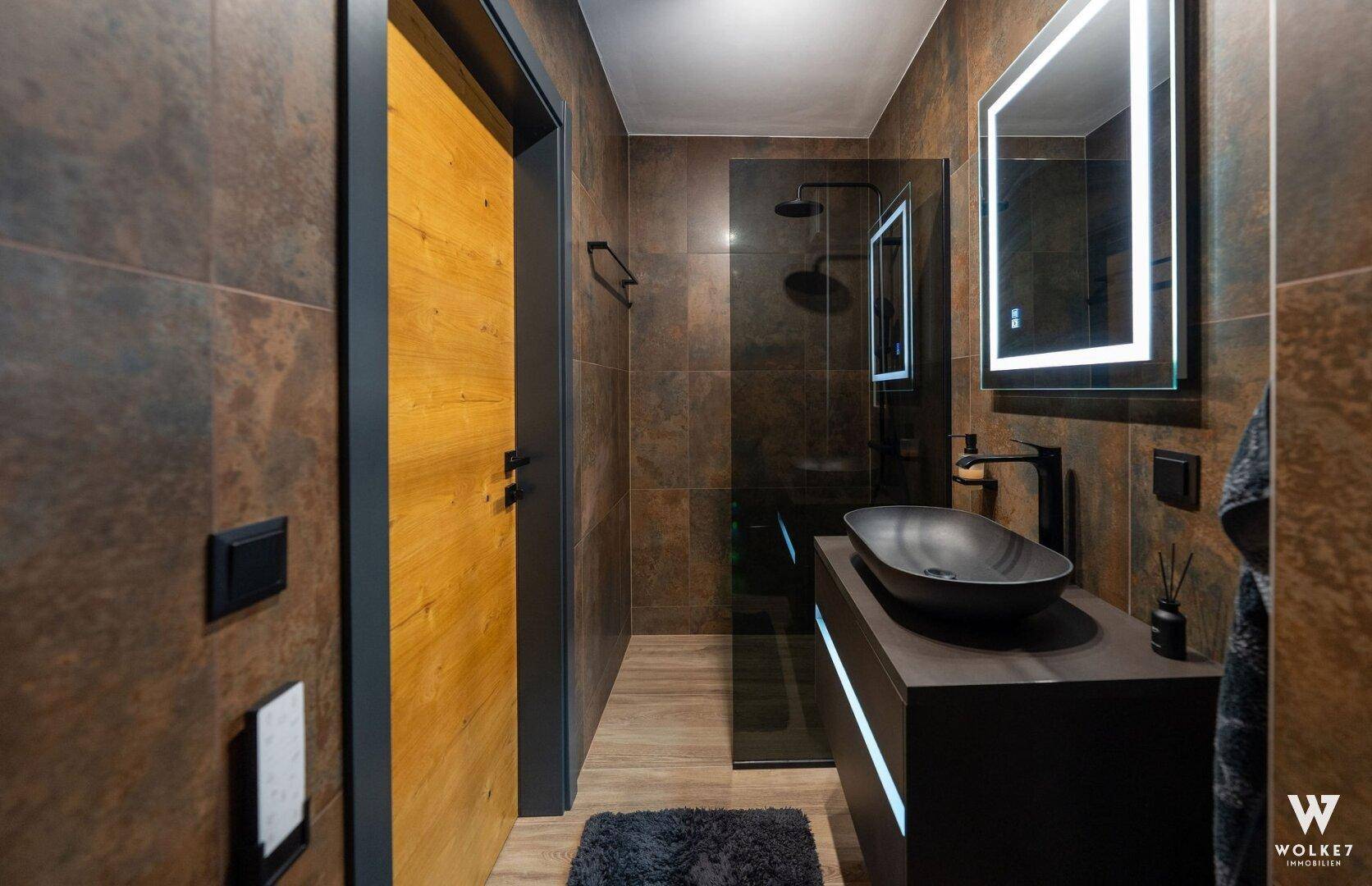 Modernes Badezimmer mit dunklen Fliesen, begehbarer Dusche und stilvollem Waschbecken.