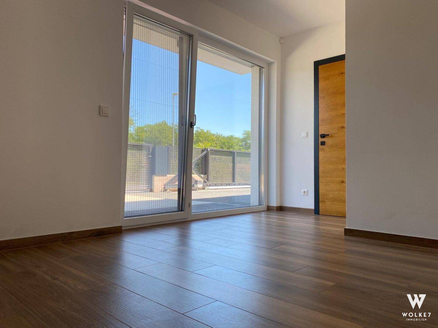 Heller Raum mit Holzboden und großer Schiebetür, die viel Tageslicht hereinlässt.