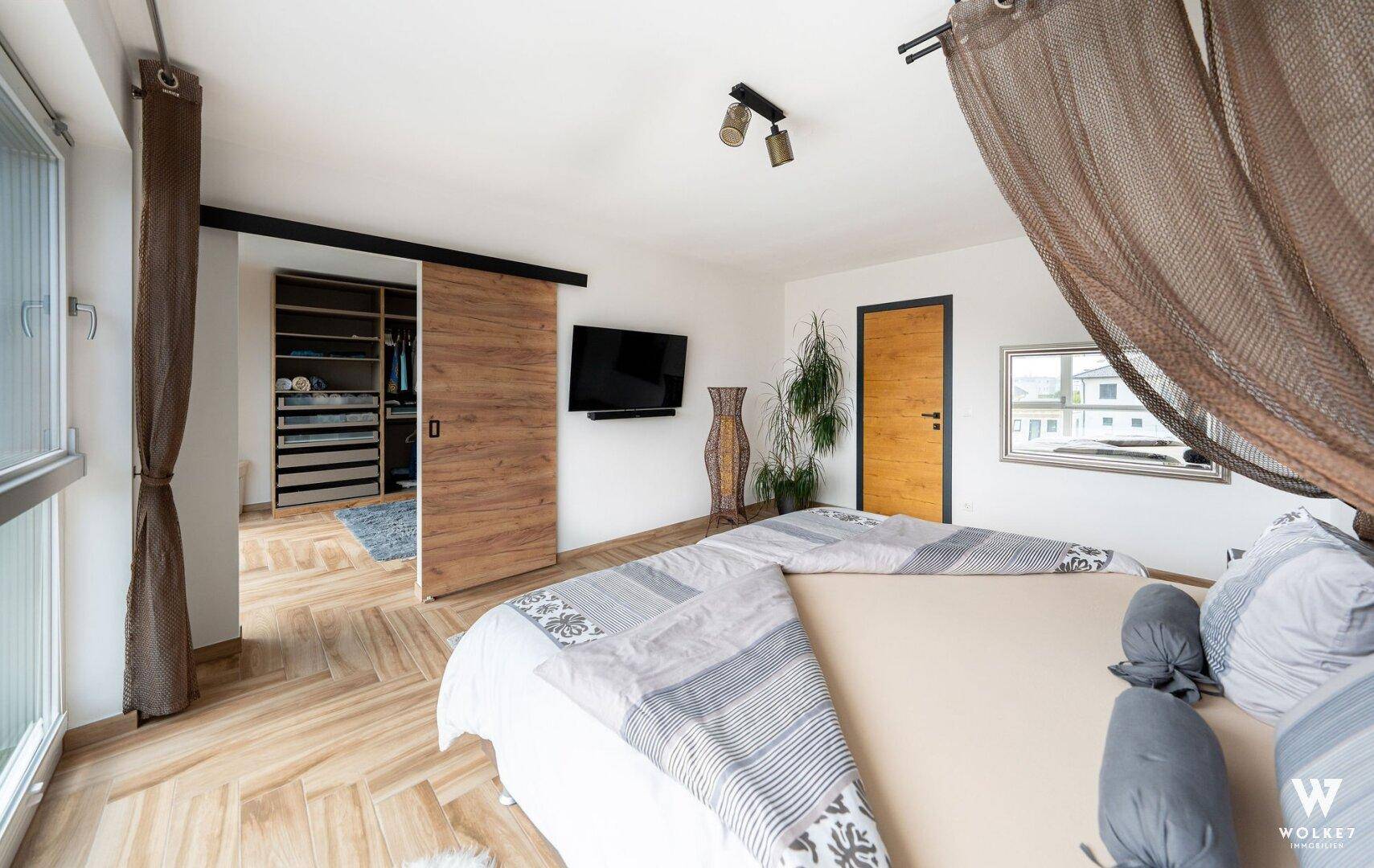 Gemütliches Schlafzimmer mit Holzboden, großem Bett und offenem Zugang zum begehbaren Kleiderschrank.