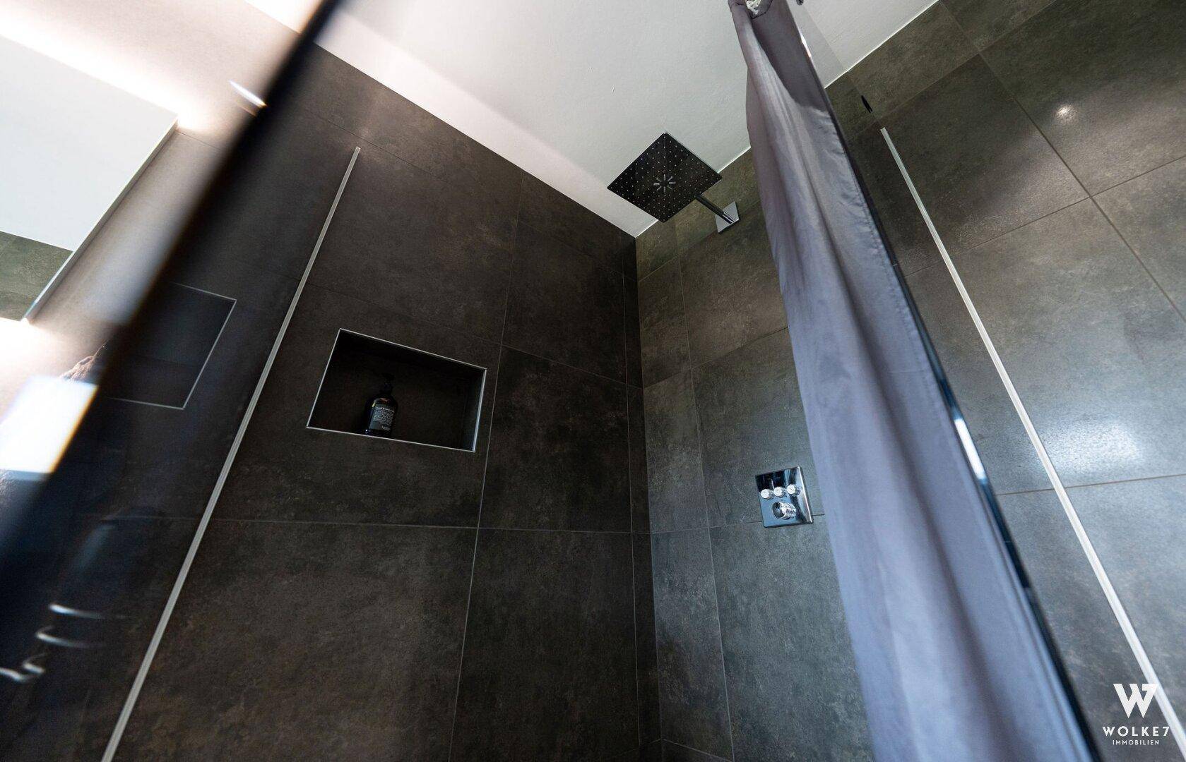 Moderne Duschkabine mit Regendusche und dunklen großformatigen Fliesen.