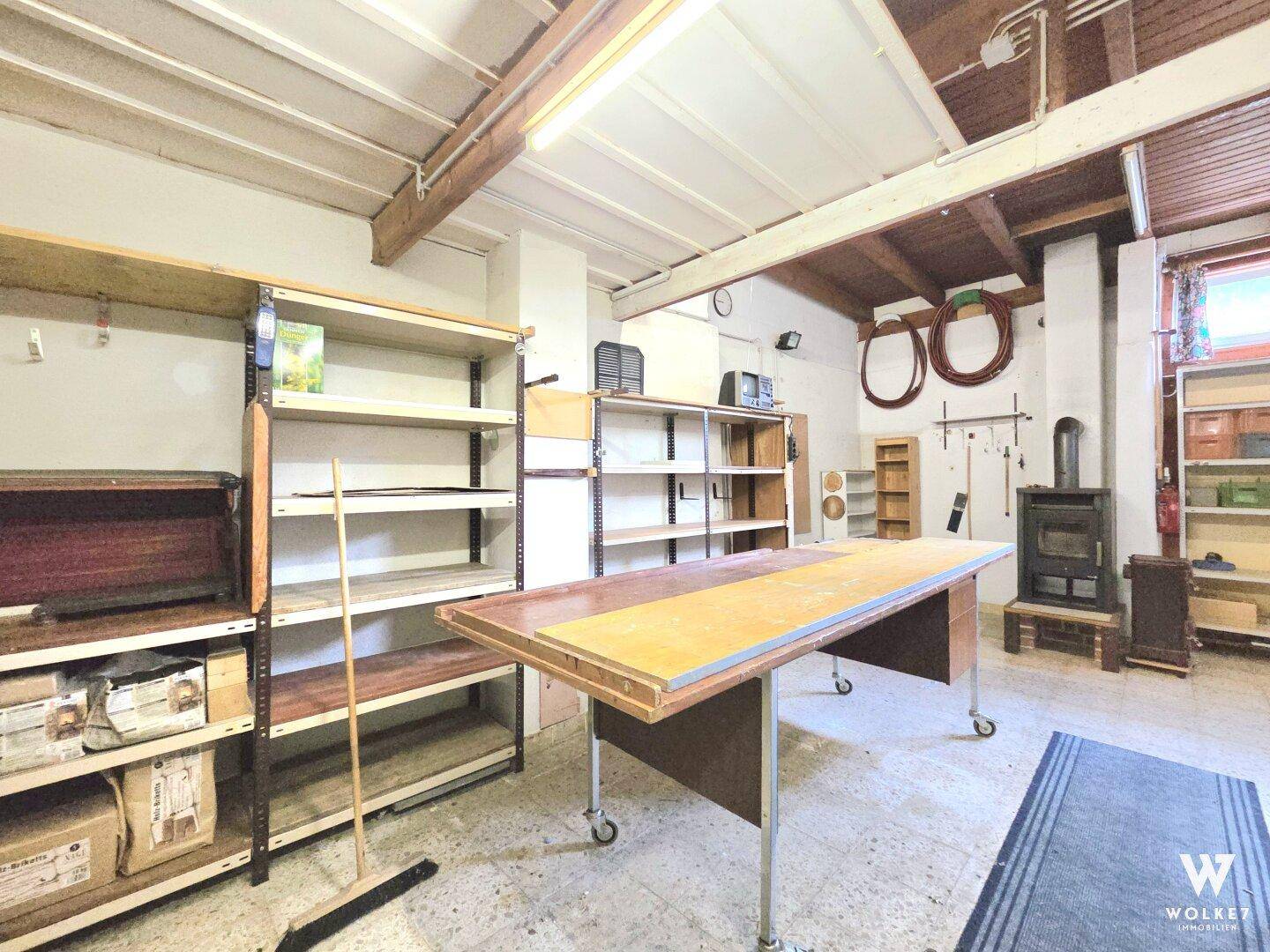 Praktischer Werkstattbereich mit Regalen, Arbeitstisch und einem gemütlichen Holzofen.