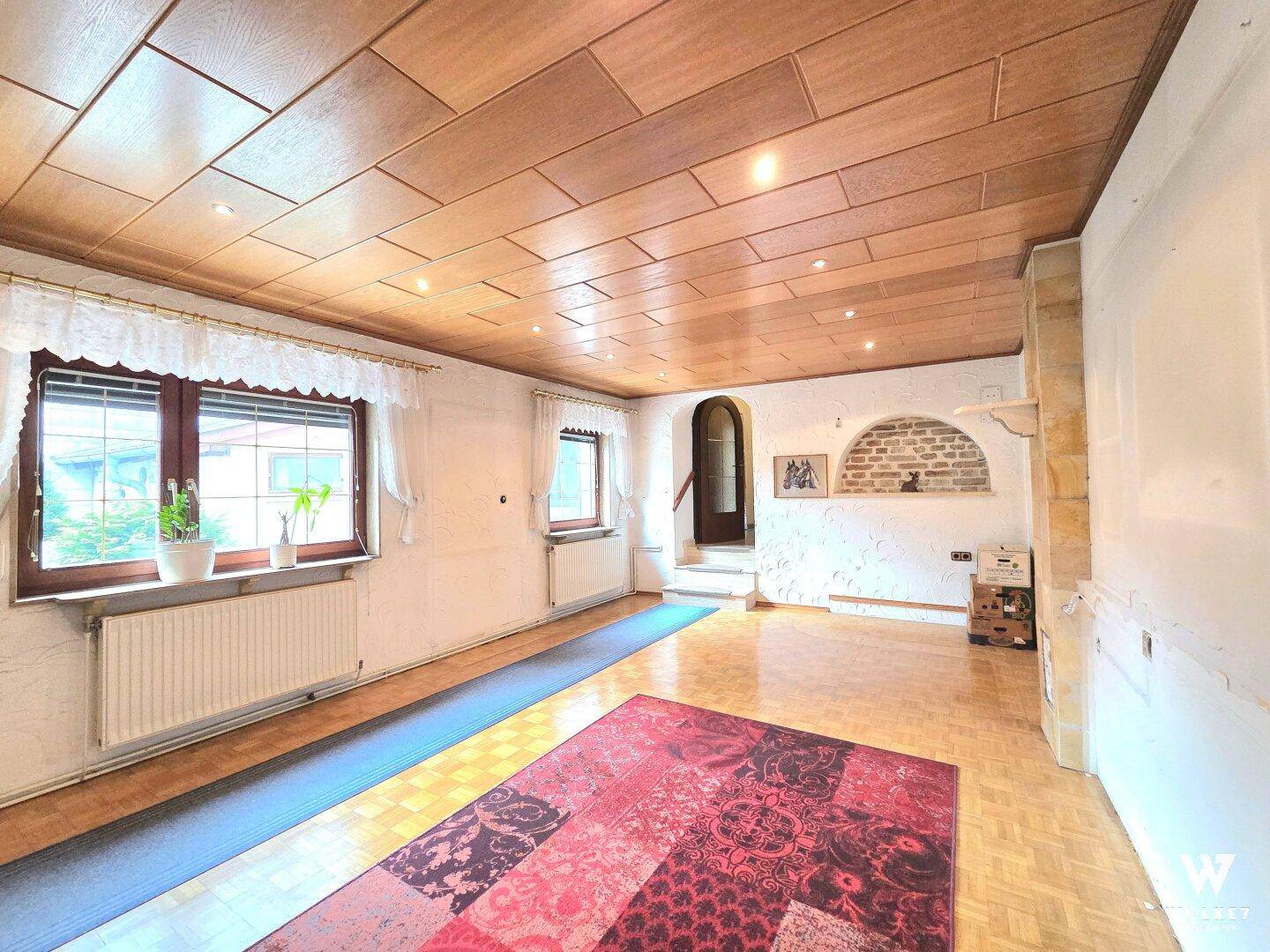 Traditionelles Wohnzimmer mit Holzdeckenverkleidung, Parkettboden und Blick nach draußen.