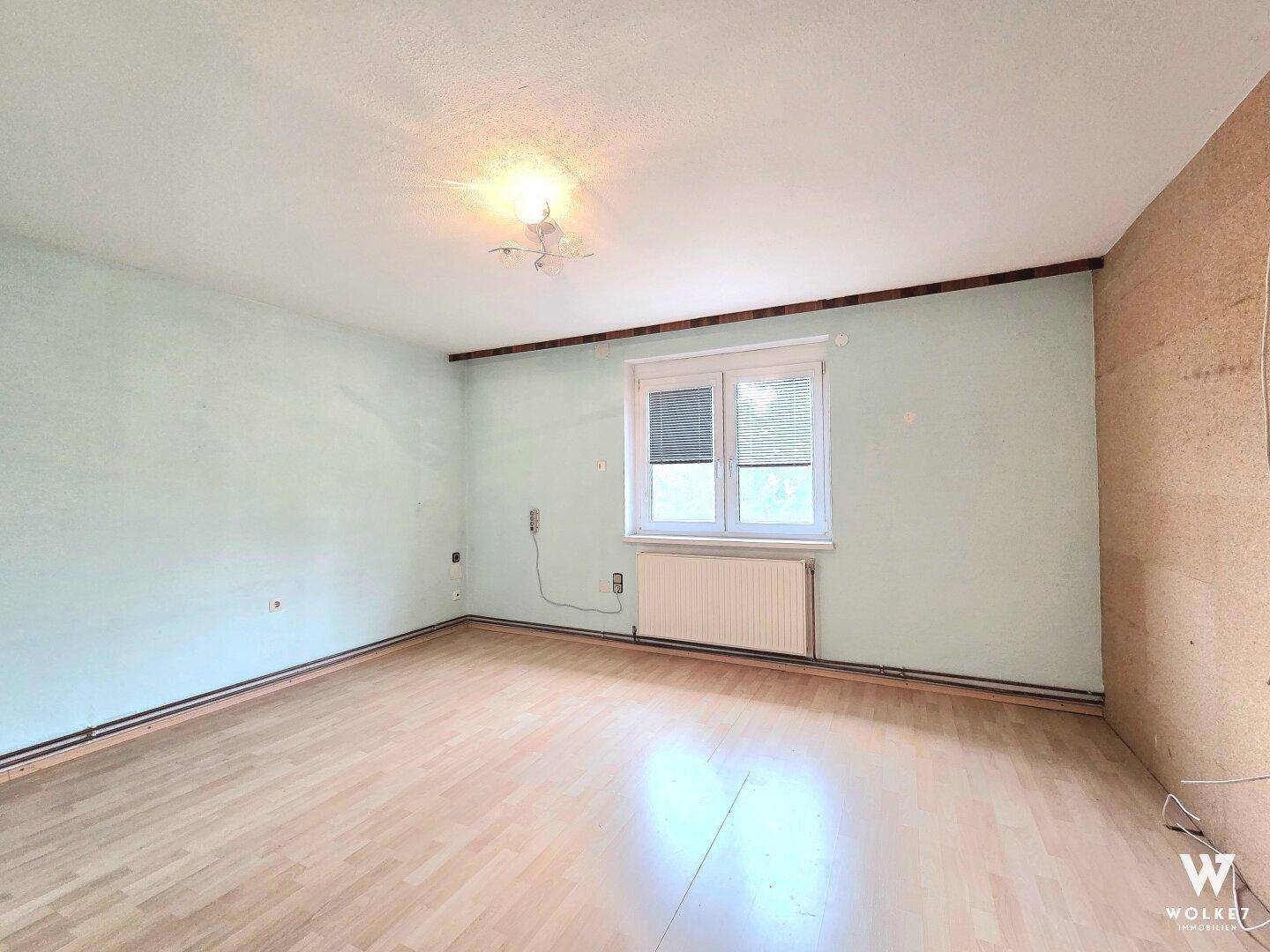 Leeres Schlafzimmer mit hellgrünen Wänden und Laminatboden, bereit zur Renovierung.