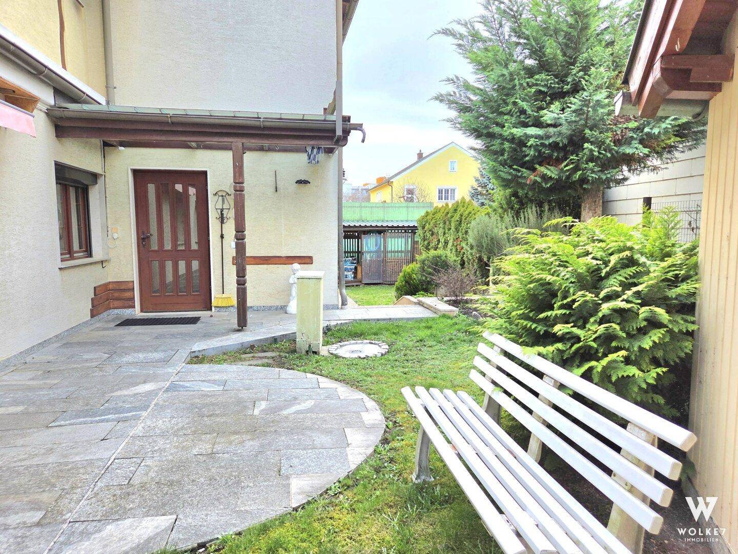 Gemütliche gepflasterte Terrasse im Garten mit Sitzbank und Zugang zum Haus.