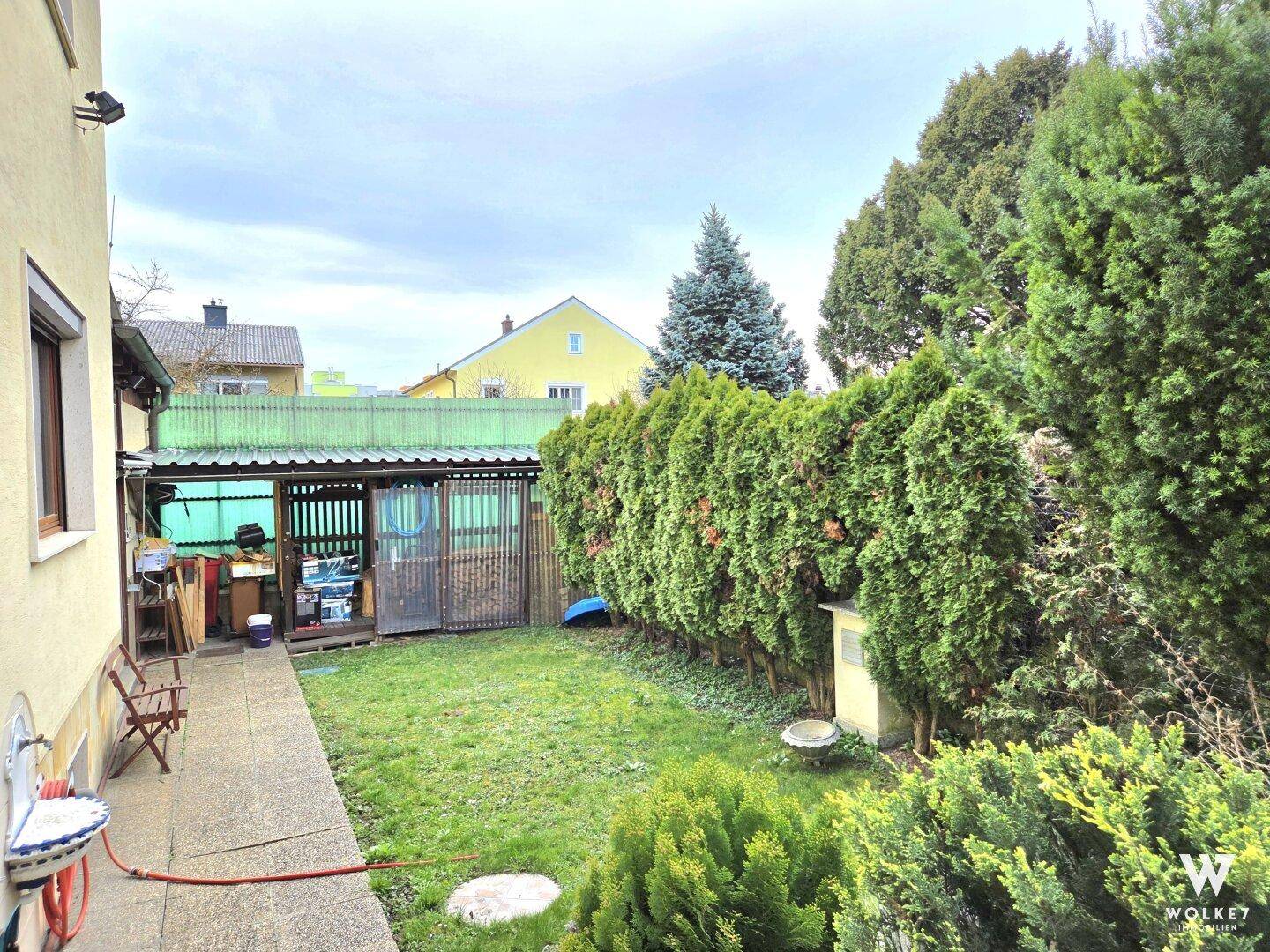 Gepflegter Gartenbereich mit Rasenfläche, hoher Hecke und praktischem Gartenhaus.