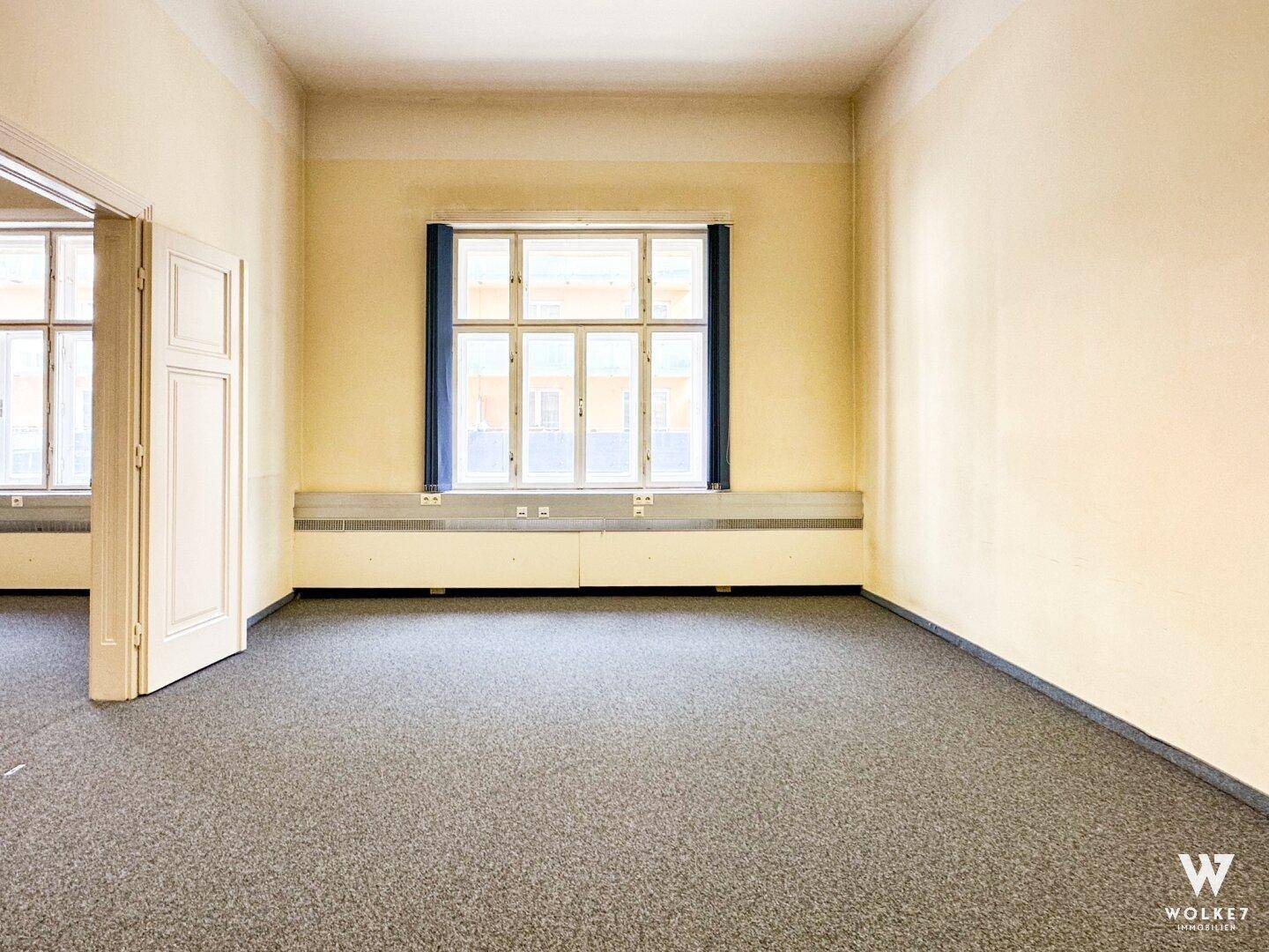 Heller, leerer Raum in einer Arztpraxis mit Teppichboden und großen Fenstern, vielseitig nutzbar.