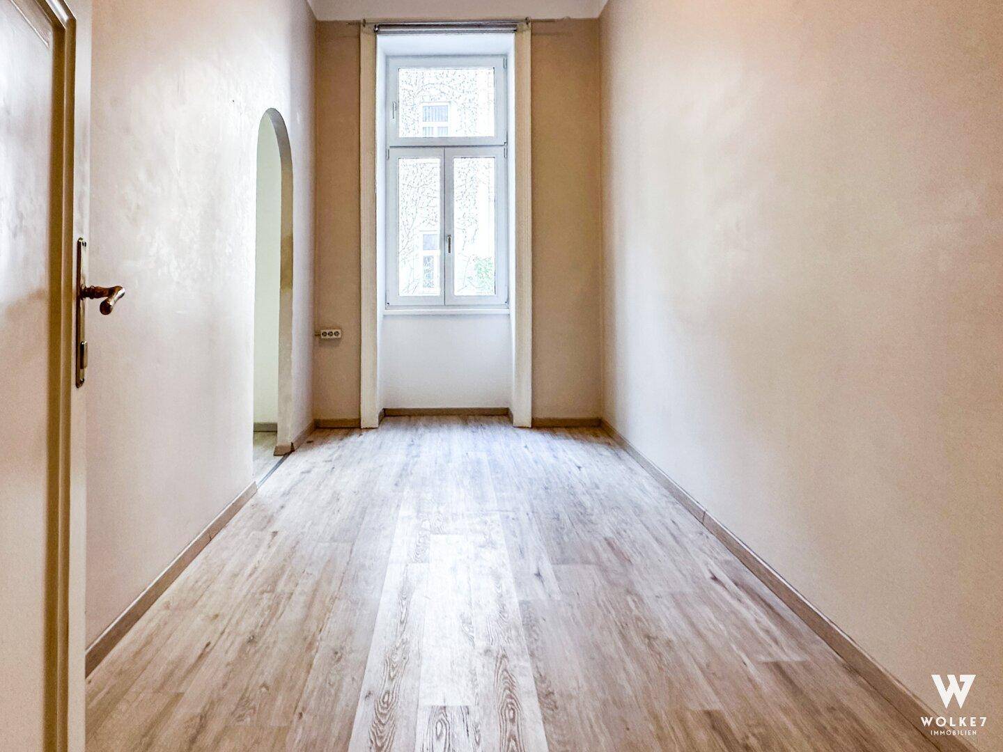 Langer, schmaler Flur mit Holzboden und einem Fenster, das Tageslicht hereinlässt, in hellem Farbton.