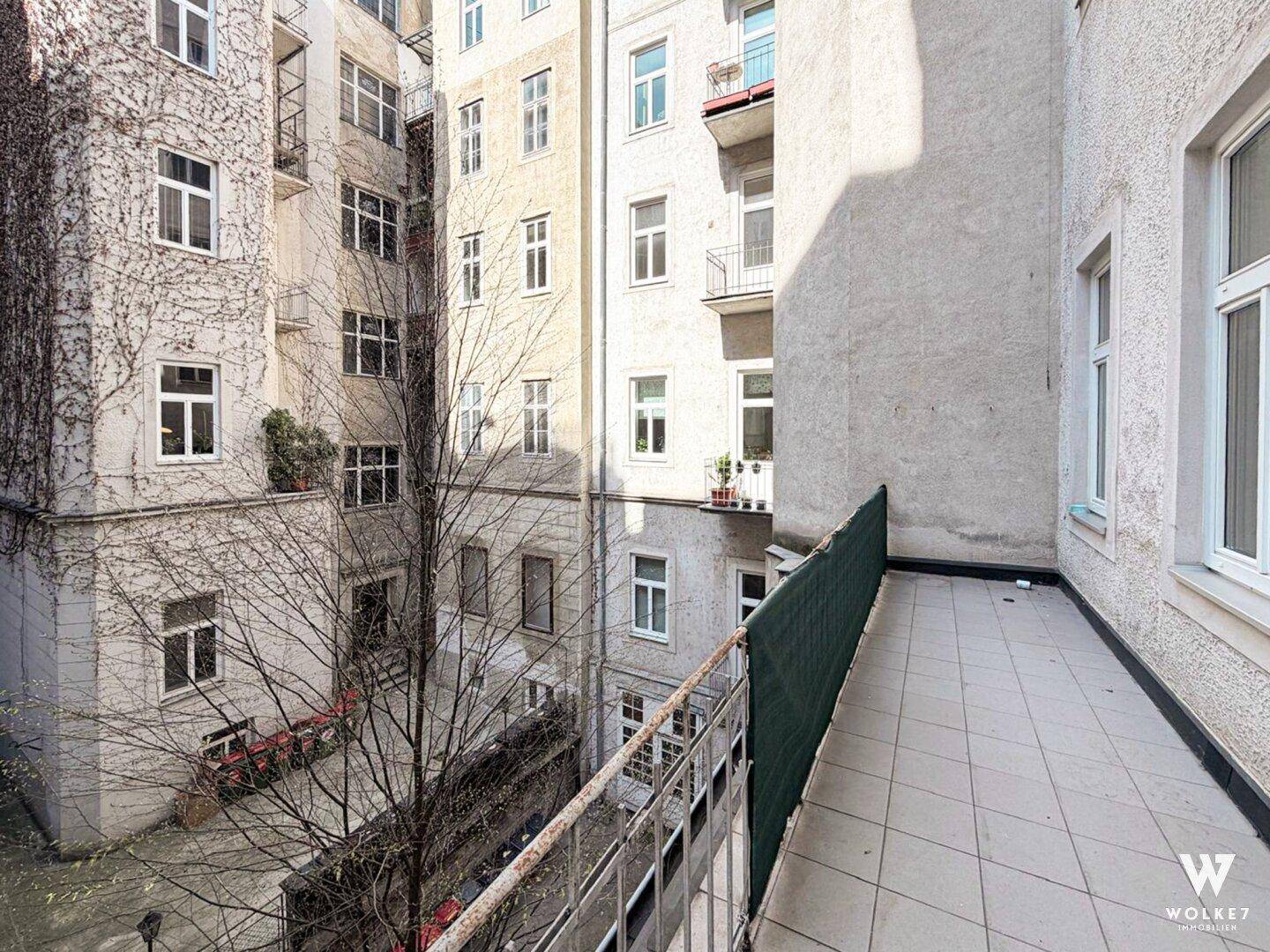 Balkon mit Blick auf einen begrünten Innenhof, umgeben von Altbauten, bietet eine ruhige Atmosphäre.