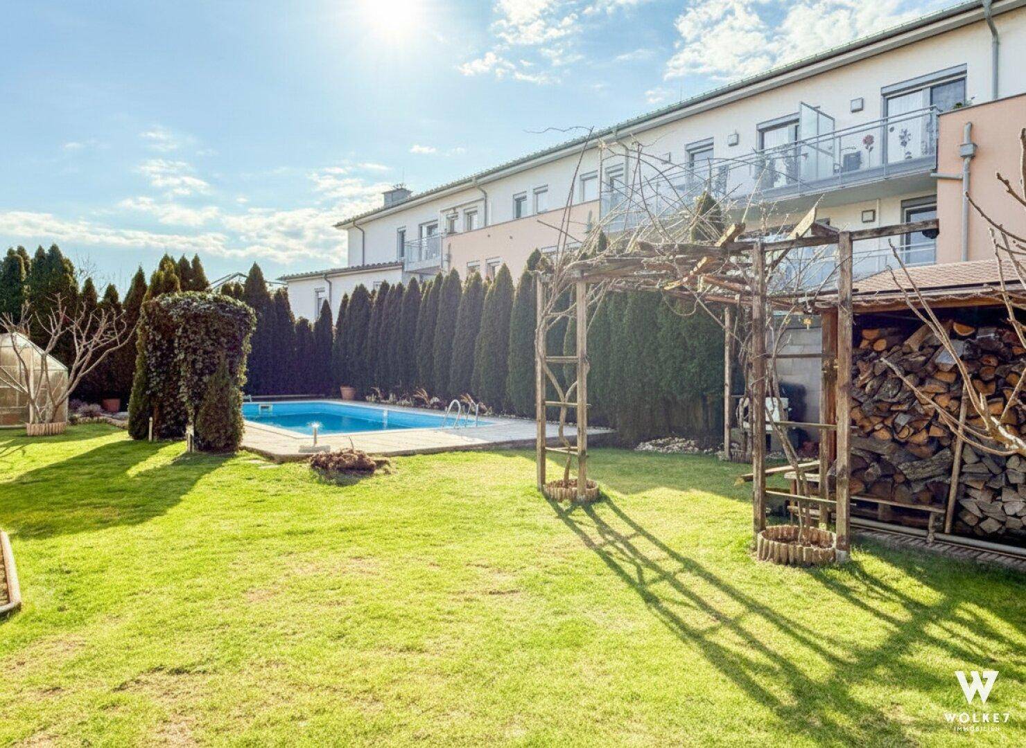 Gepflegter Garten mit Swimmingpool, Rasenfläche und Holzschuppen unter blauem Himmel.