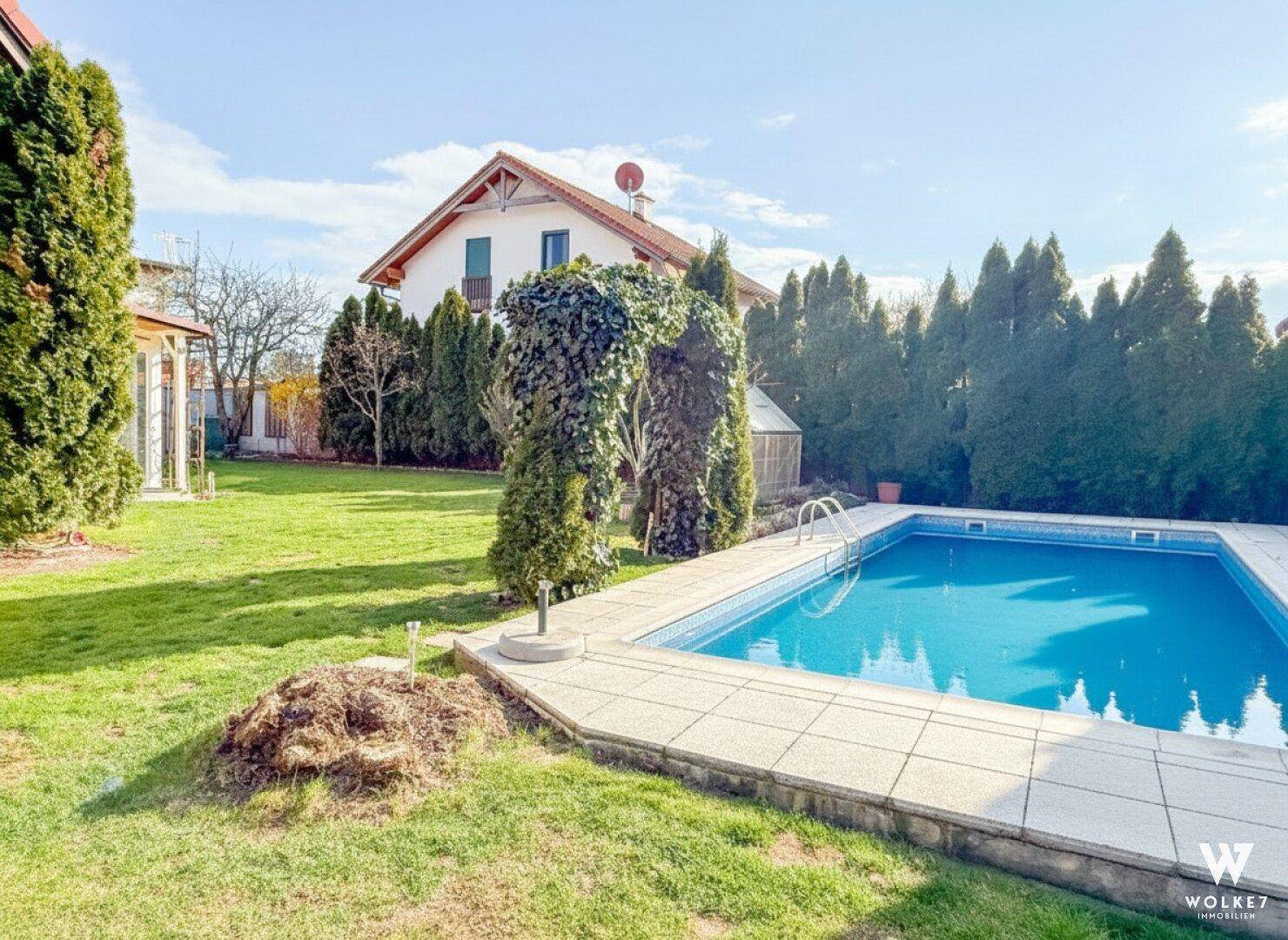 Großer Garten mit blauem Swimmingpool und einem charmanten Haus im Hintergrund.