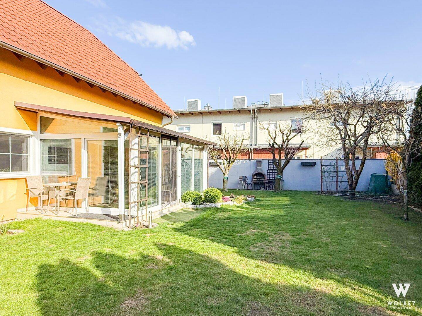 Garten mit verglastem Wintergarten, Grillplatz und gepflegter Rasenfläche am Haus.