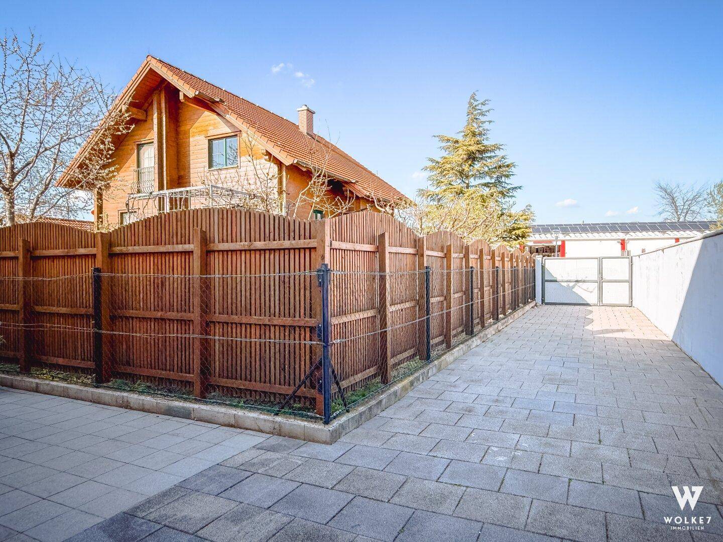Lange gepflasterte Einfahrt neben einem Holzzaun, führt zu einem charmanten Holzhaus.
