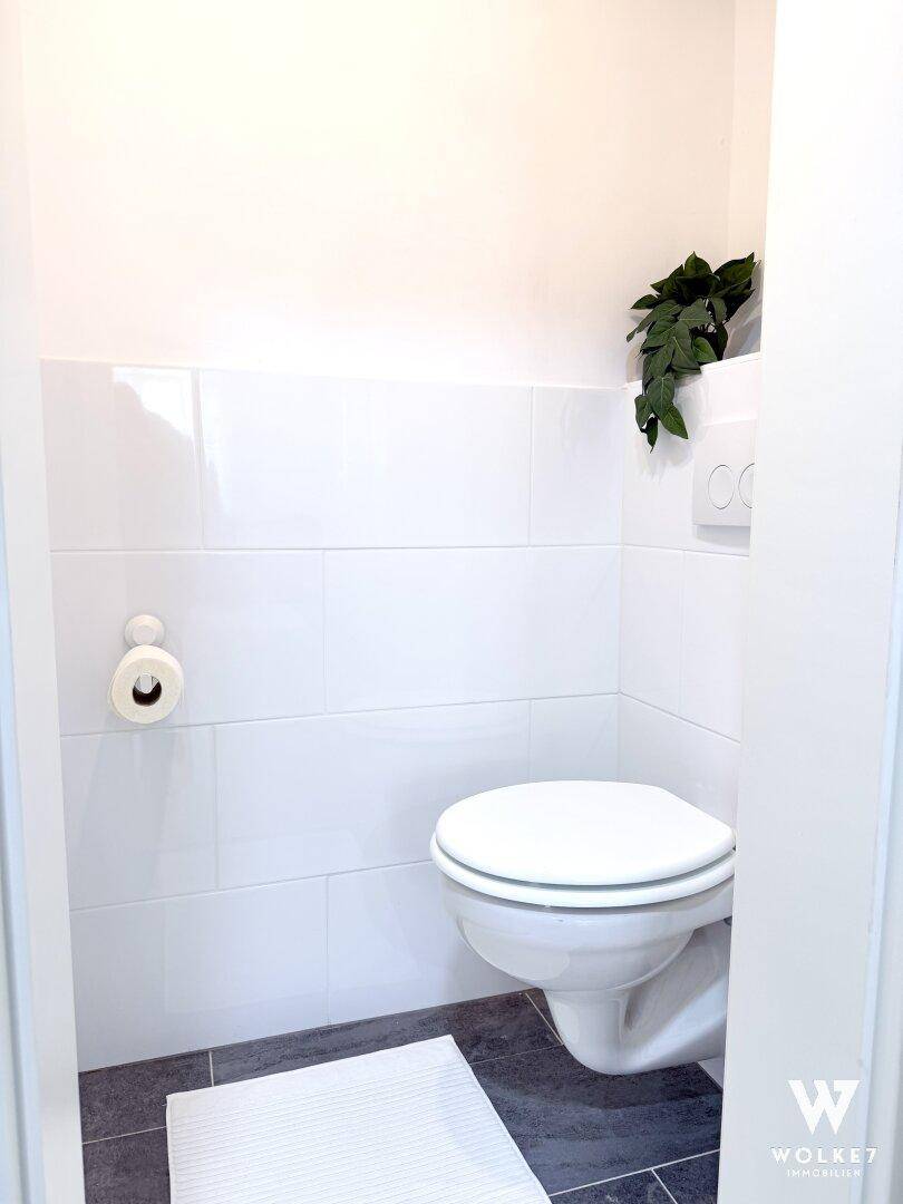 Separates WC mit Wand-WC und weißen Fliesen, sauber und minimalistisch.