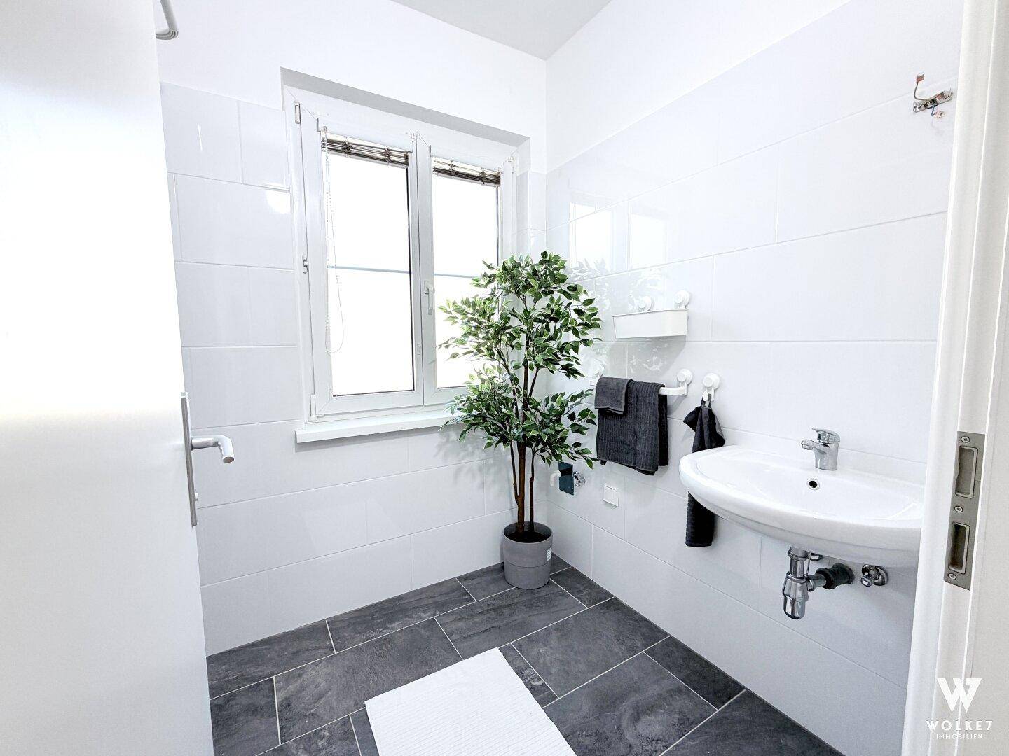 Modernes Badezimmer mit Waschbecken, Spiegel und großem Fenster für Tageslicht.