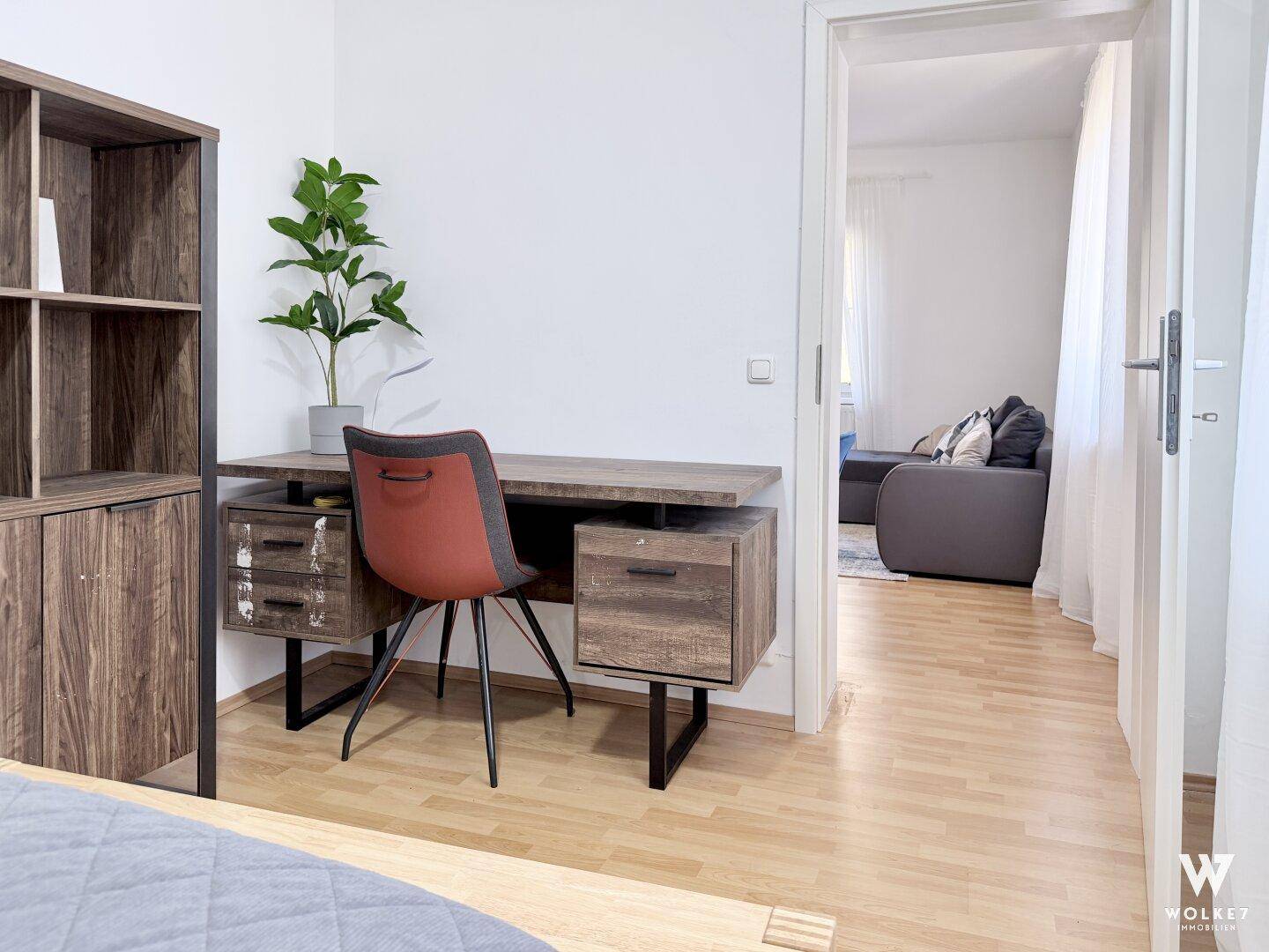 Arbeitsbereich mit Schreibtisch und Regal, verbunden mit dem Wohnzimmer.