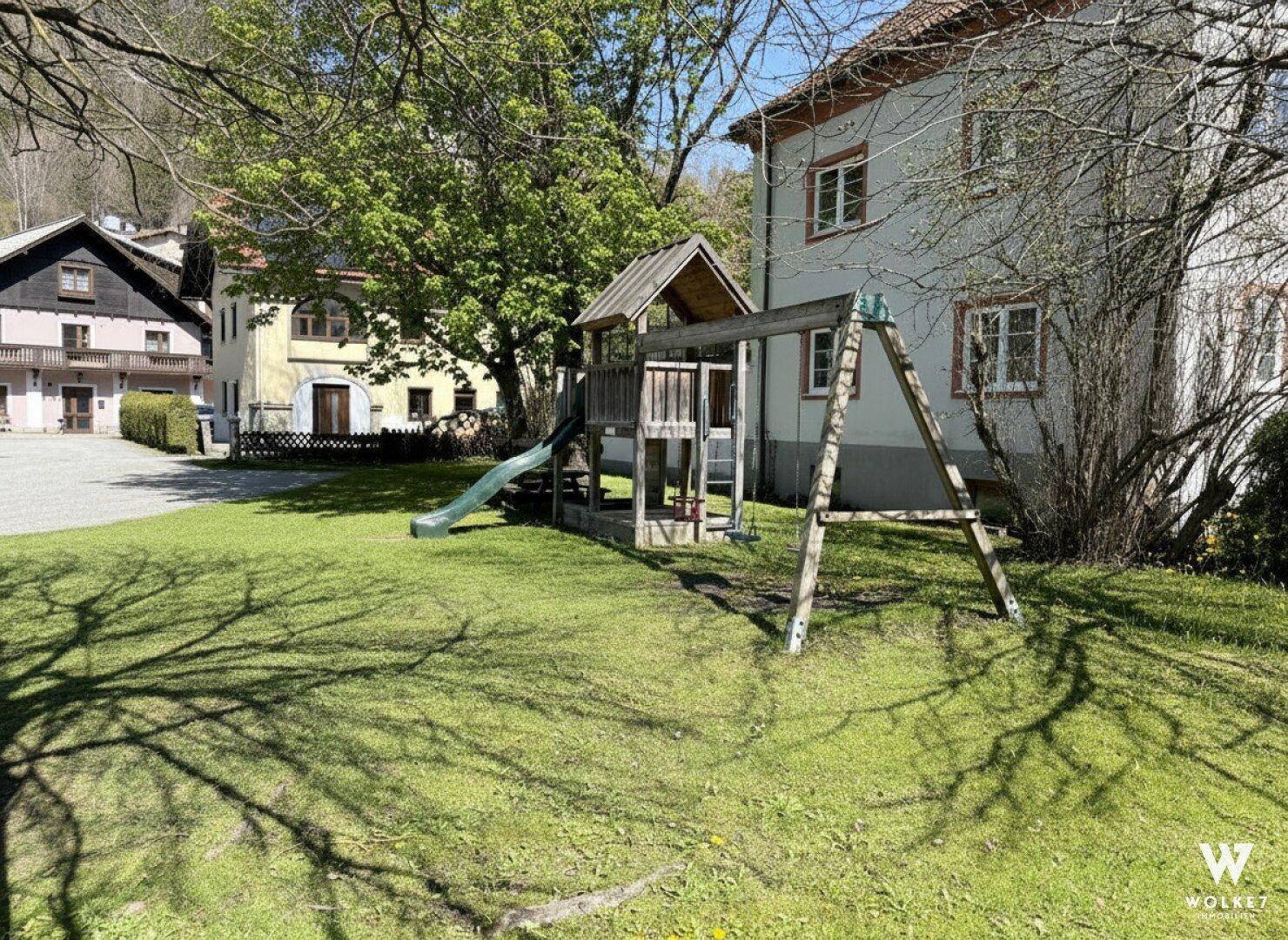 Großer Gartenbereich mit Kinderspielplatz und Schaukeln vor dem Gebäude.