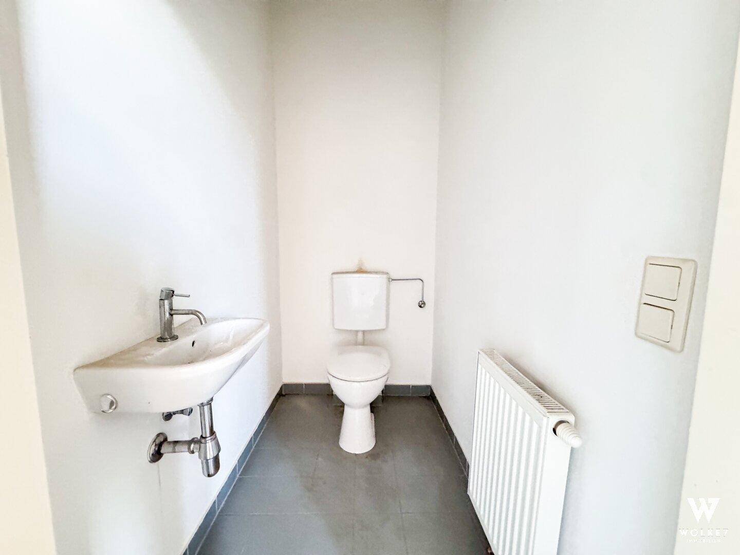 Kleines Gäste-WC mit Waschbecken, Toilette und Heizkörper, ausgestattet mit grauen Bodenfliesen.