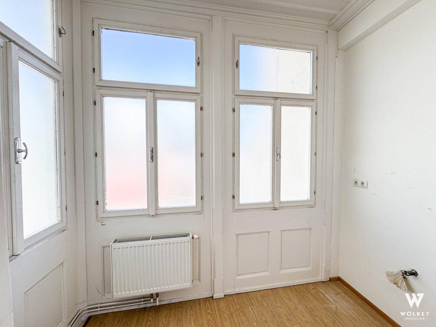 Kleiner Raum mit hohen Fenstern und Heizkörper, bereit für Renovierung oder individuelle Nutzung.