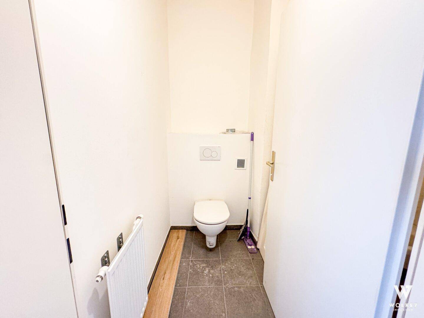 Separate Toilette mit Wand-WC und Fliesenboden, schlicht und funktional gestaltet.