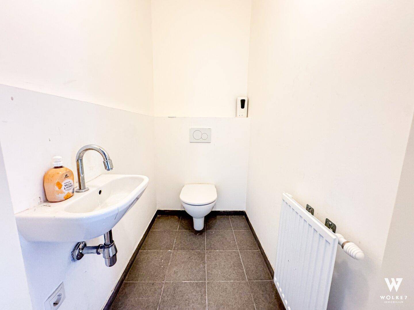 Separate Toilette mit Waschbecken, Wand-WC und Fliesenboden, sauber und hell.