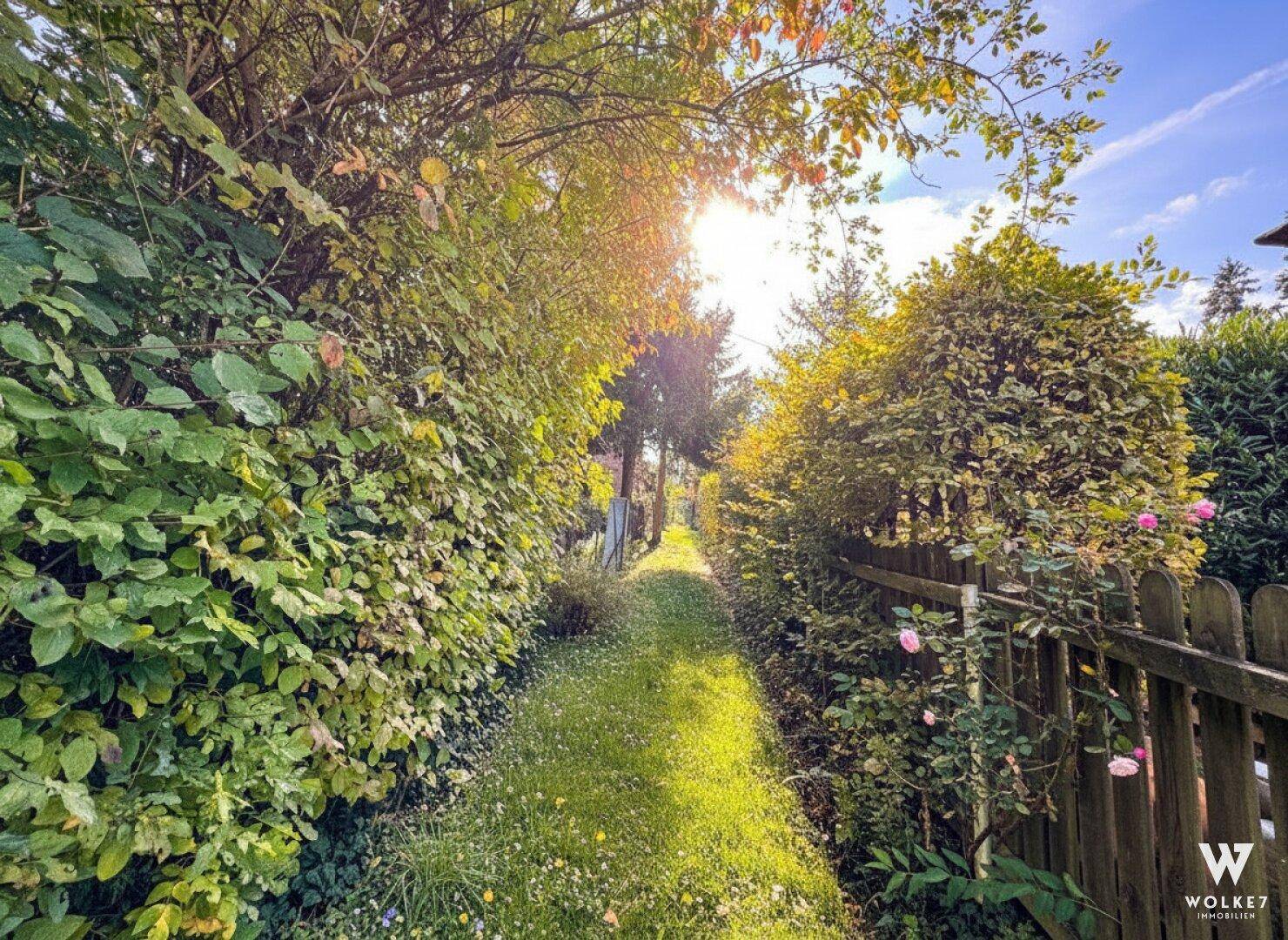 Schmaler Gartenweg umgeben von dichtem Grün und Hecken, durch den die Sonne scheint.