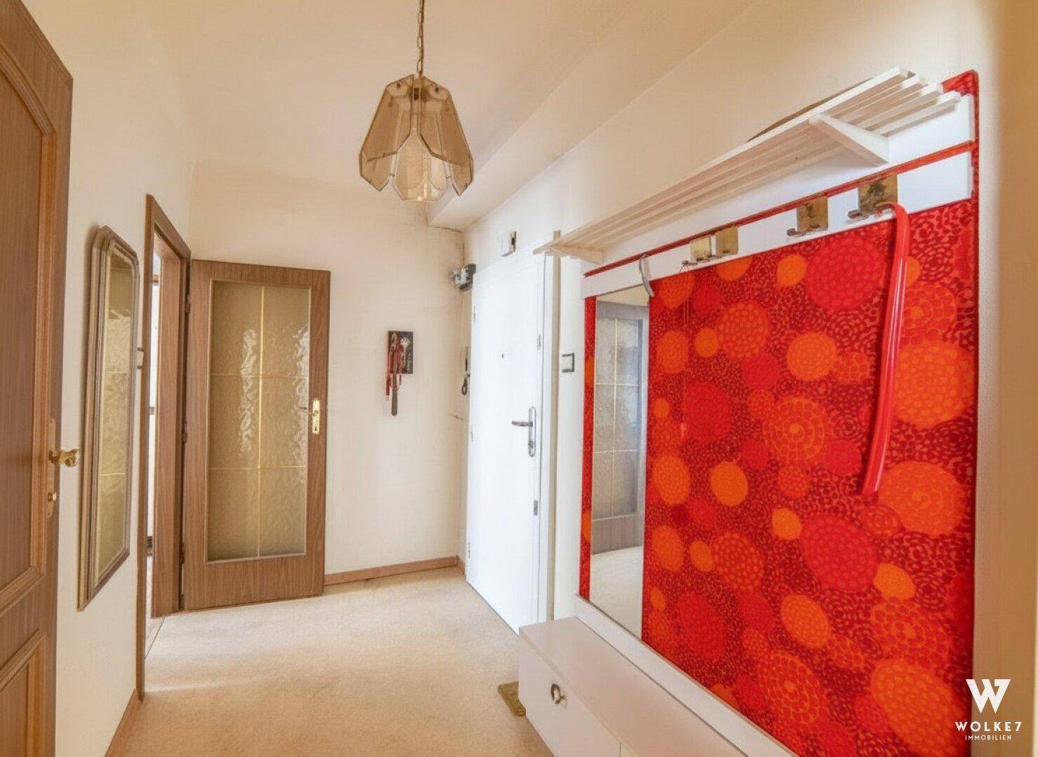 Heller Flur mit Teppichboden, einer bunten Garderobe und mehreren Holztüren, die zu den Zimmern führen.
