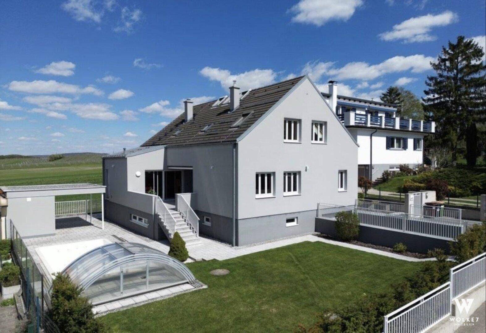 Modernes Einfamilienhaus mit großem Garten, Rasenfläche und überdachtem Poolbereich.