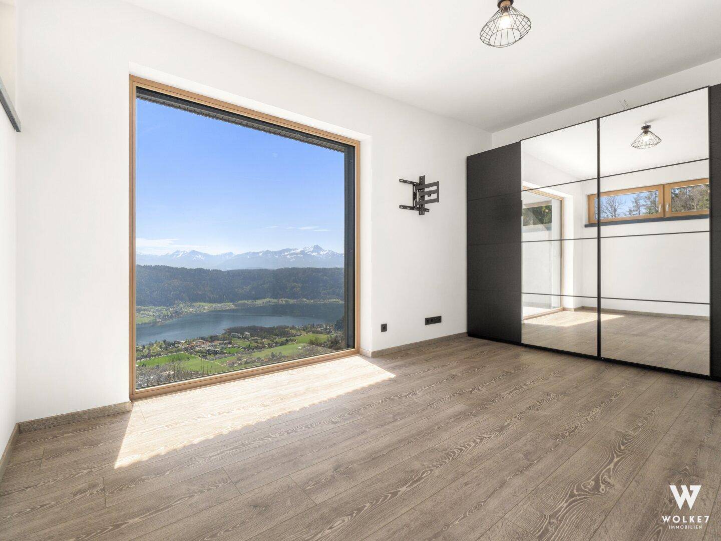 Helles Schlafzimmer mit großem Fenster, das einen beeindruckenden Blick auf den See und die Berge freigibt.