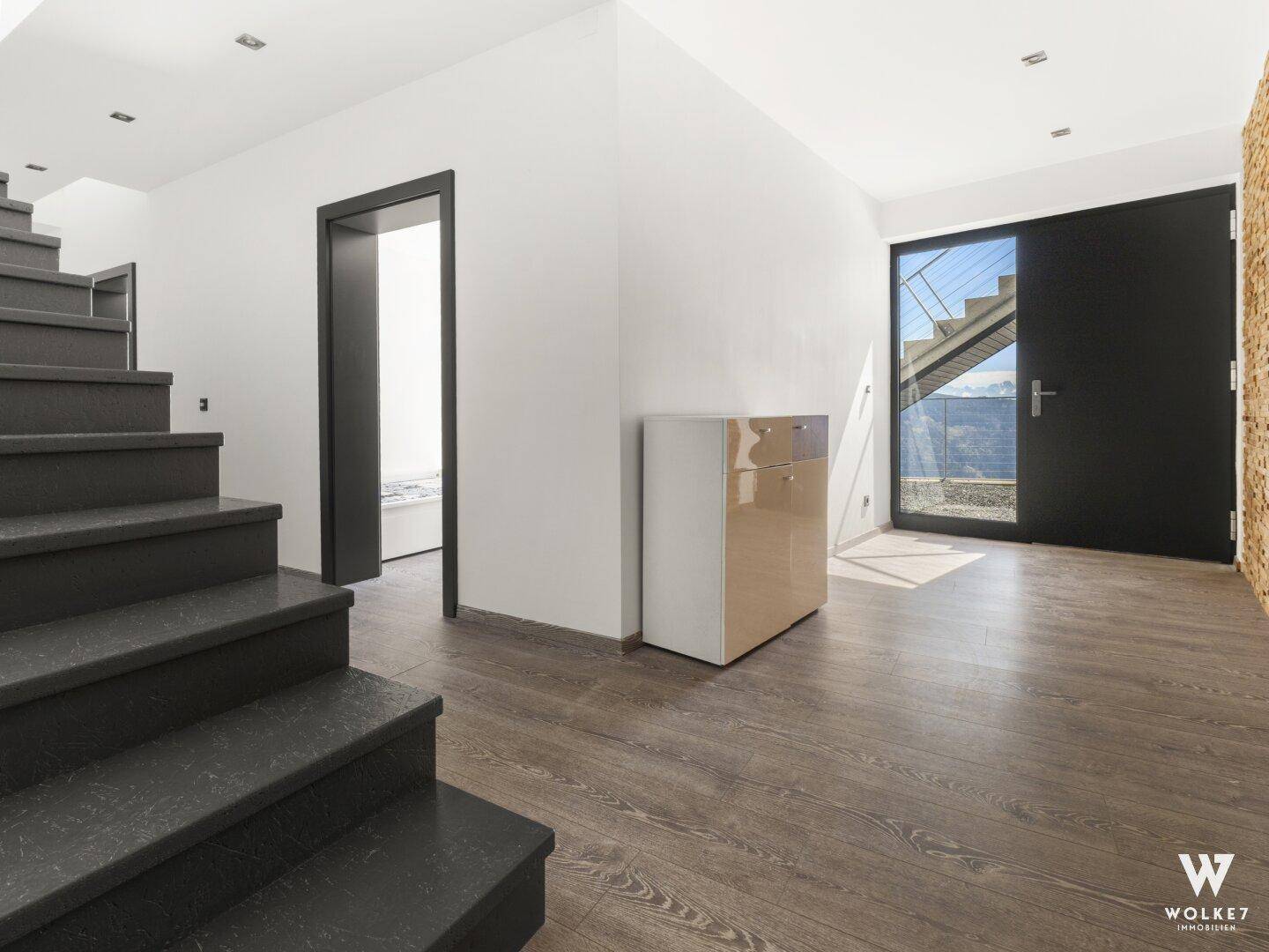 Heller Eingangsbereich mit Treppe und moderner Haustür, die den Blick nach draußen freigibt.