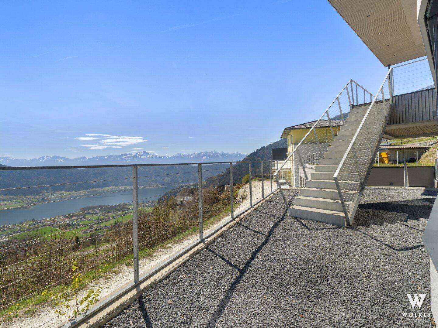 Außenbereich mit Kiesweg und Treppe, die zu einem atemberaubenden Blick auf den See und die Berge führt.