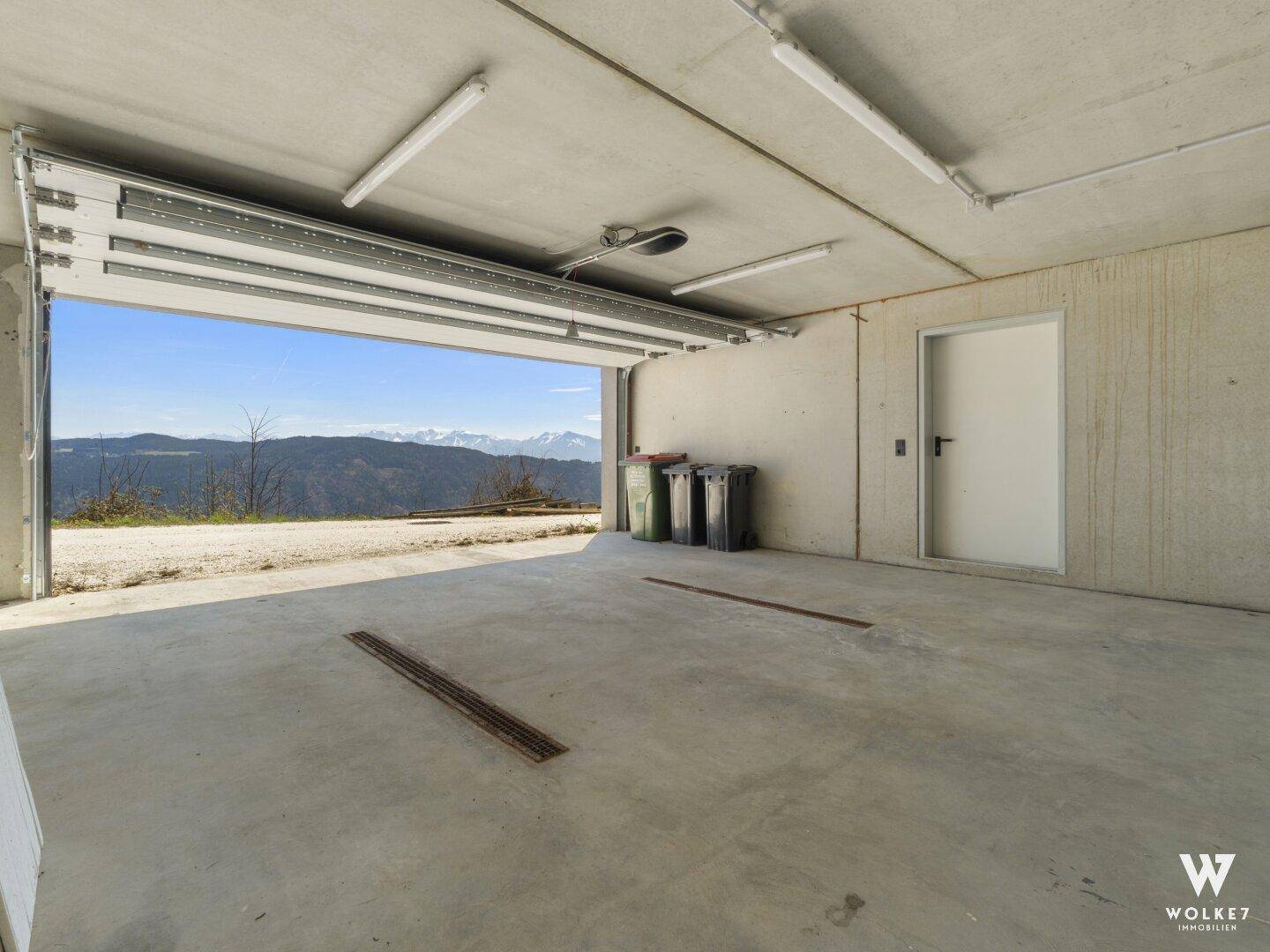 Geräumige Garage mit Betonboden und offenem Tor, das einen weiten Blick auf die Berge bietet.