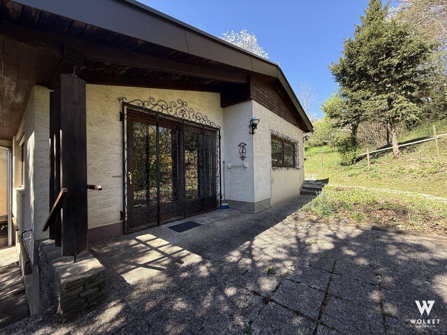 Seitenansicht des Hauses mit dekorativen Fenstern und Zugang zum Gartenbereich.