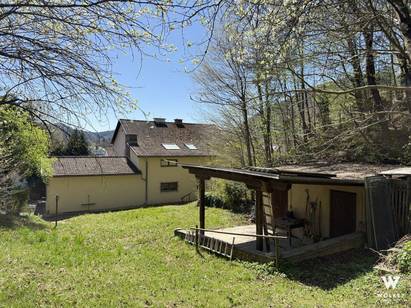 Gartenbereich mit Rasen, einem Holzschuppen und dem Haupthaus im Hintergrund.