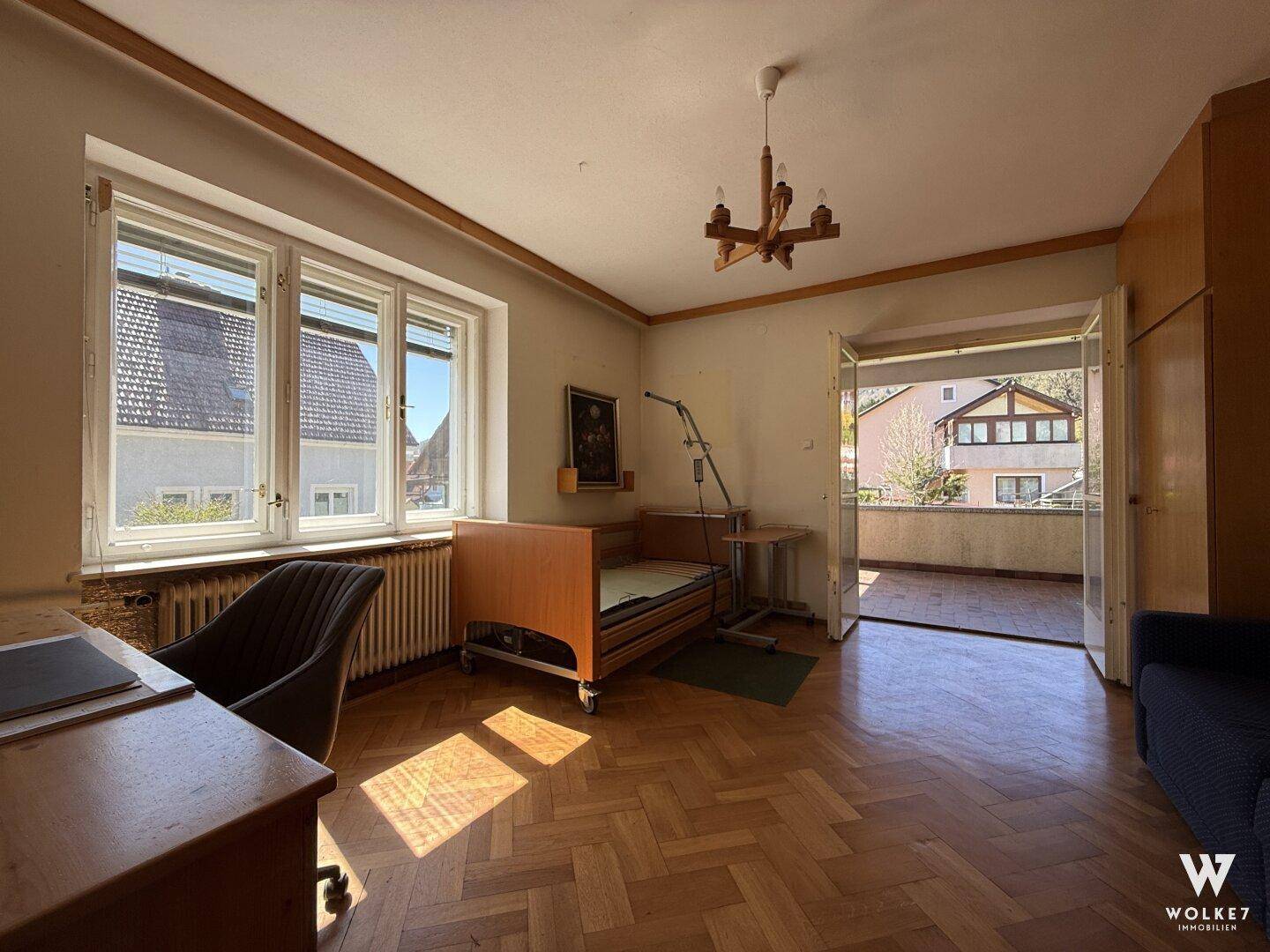 Helles Schlafzimmer mit Parkettboden, Zugang zum Balkon und Blick ins Grüne.