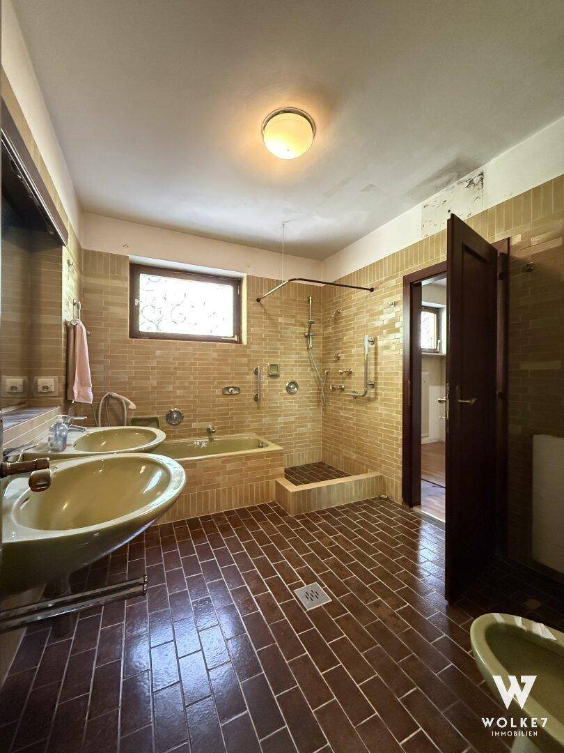 Großes Badezimmer im 80er-Jahre-Stil mit Doppelwaschbecken, Badewanne, Dusche und Fenster.
