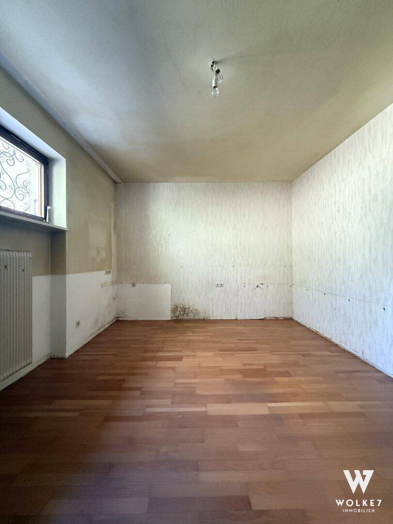 Leeres Schlafzimmer mit Holzboden, Fenster und Heizkörper, bereit zur Renovierung.