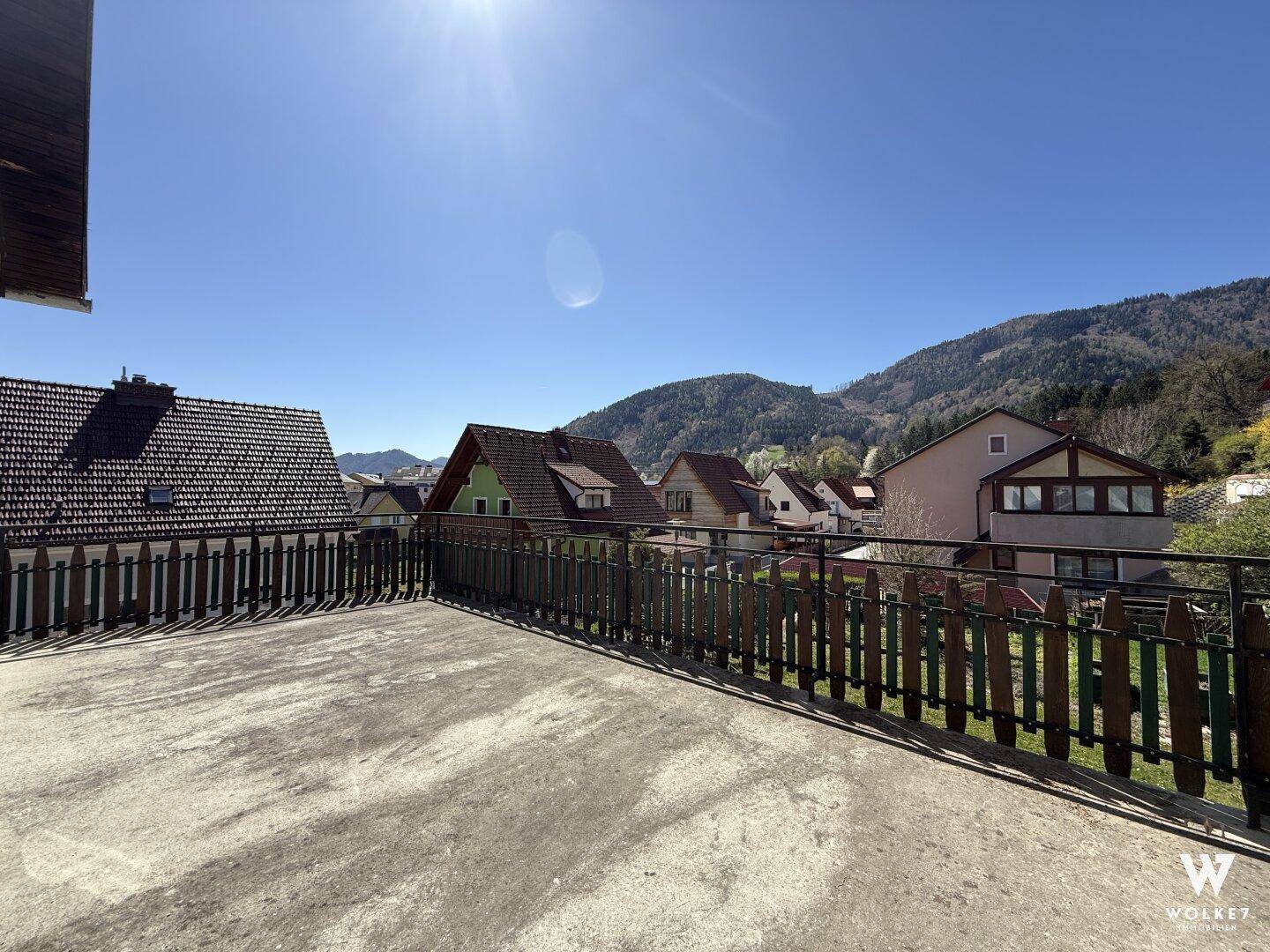 Großer, sonniger Balkon mit weitem Blick auf die umliegende Landschaft und Häuser.