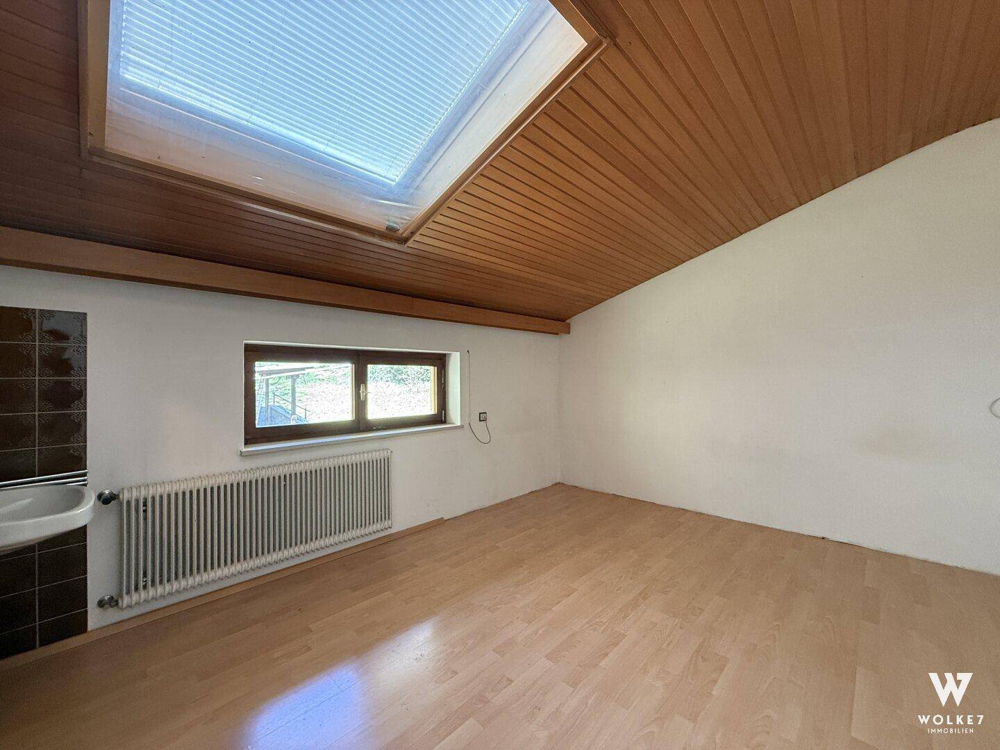 Dachgeschosszimmer mit Holzdecke, Dachfenster, kleinem Waschbecken und Ausblick.