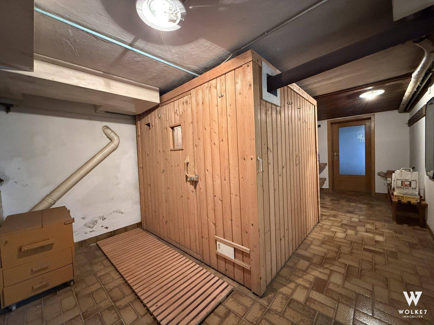 Wellnessbereich im Keller mit einer großen Saunakabine und Fliesenboden.