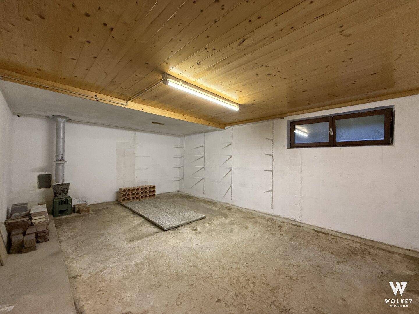 Kellerraum mit Betonboden, Regalen und Fenster, ideal als Lagerfläche.