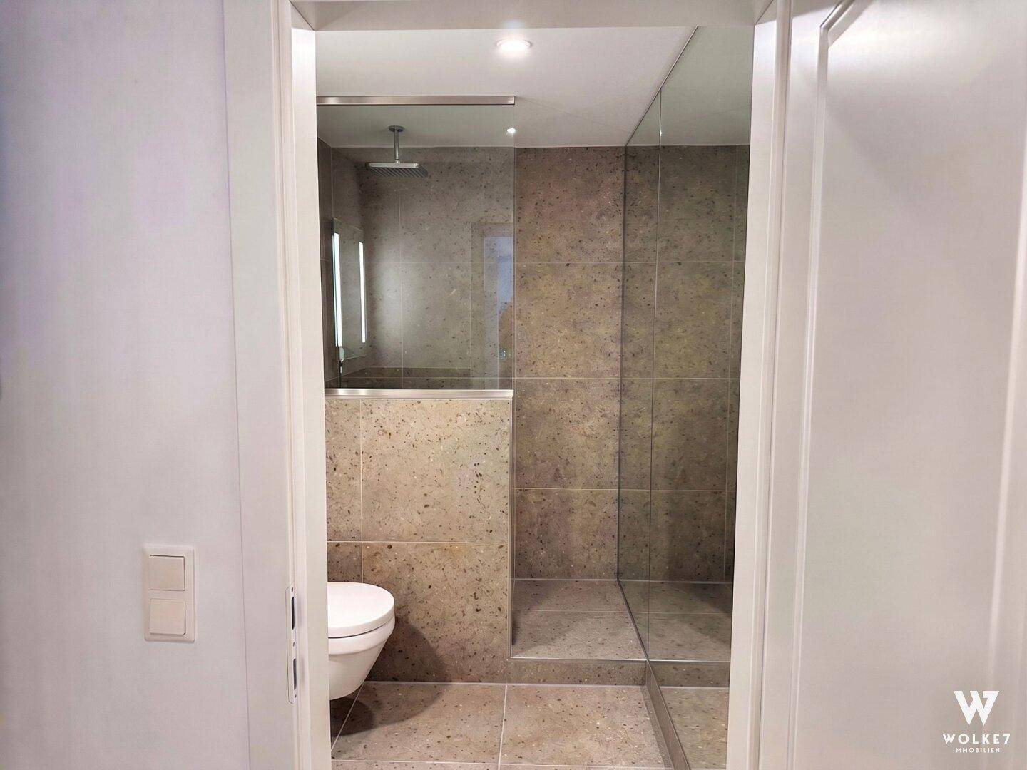 Modernes Badezimmer mit begehbarer Dusche, Wand-WC und großformatigen Fliesen.