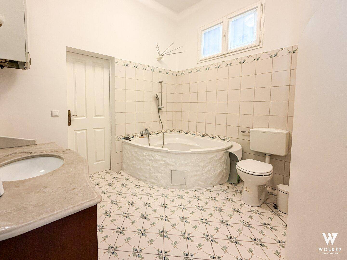 Badezimmer mit Eckbadewanne, WC und gefliesten Wänden und Boden im 80er-Jahre-Stil.